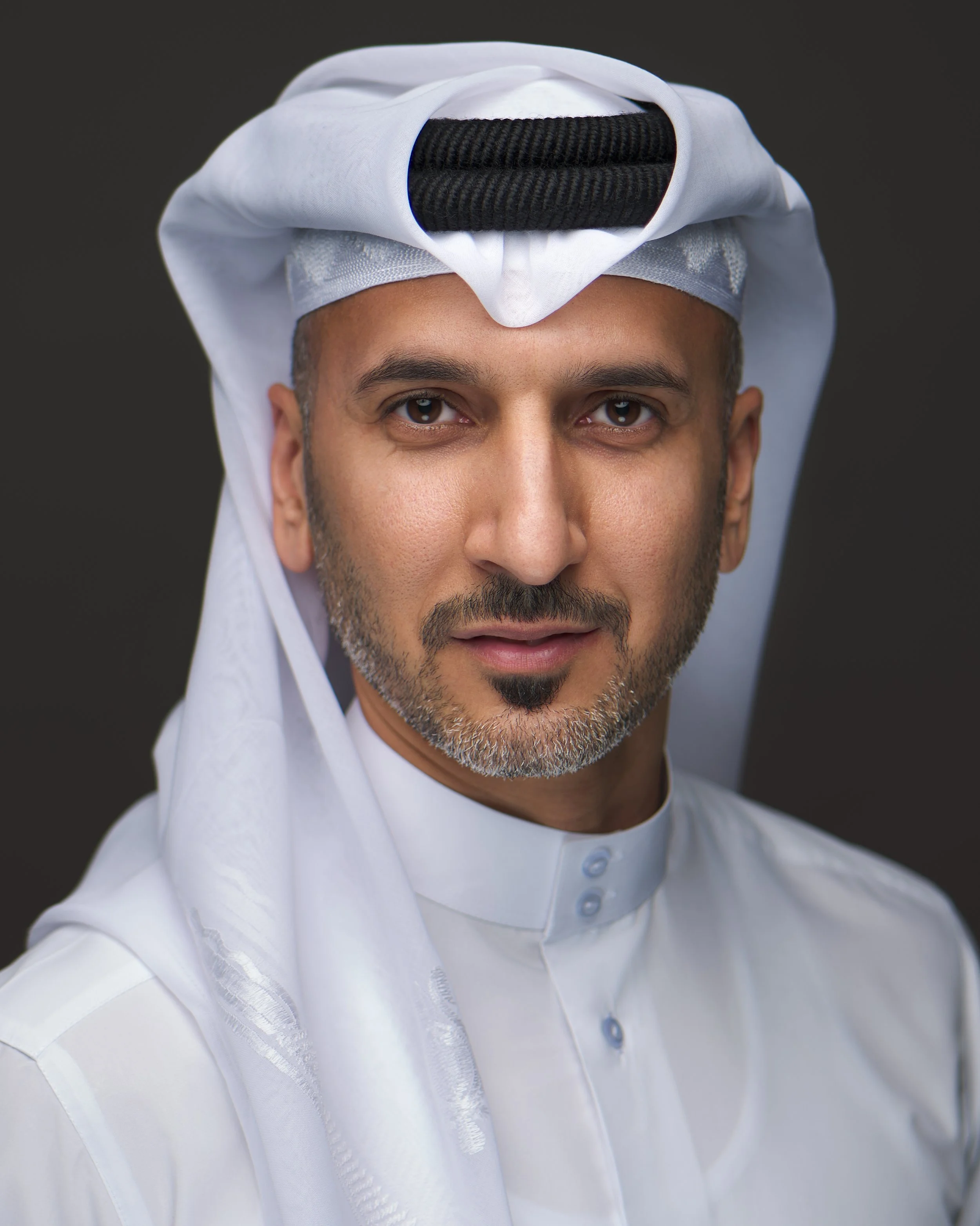 A man wearing traditional Middle Eastern attire, including a white thobe and a white ghutra with an agal, looking at the camera with a neutral expression.