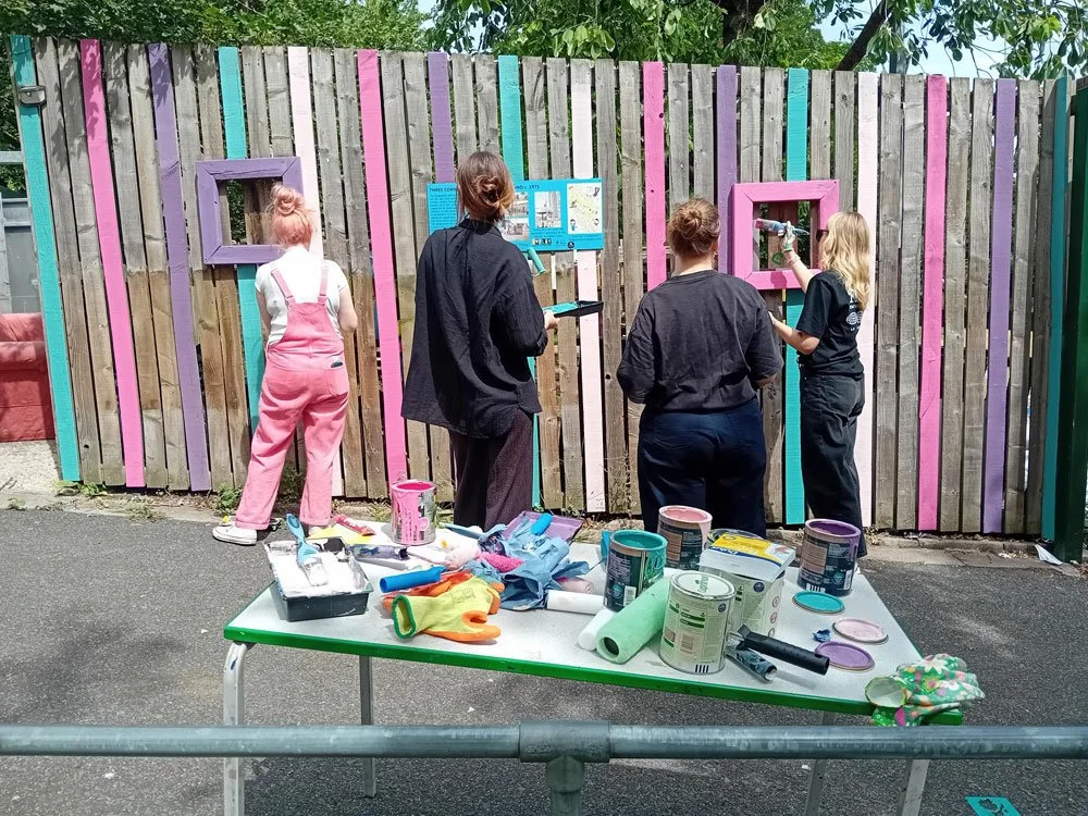 Four volunteers painting a wooden fence