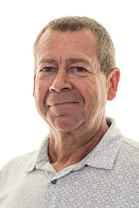 Portrait of a middle-aged man with short brown hair, wearing a light-colored checkered shirt, looking at the camera with a neutral expression.
