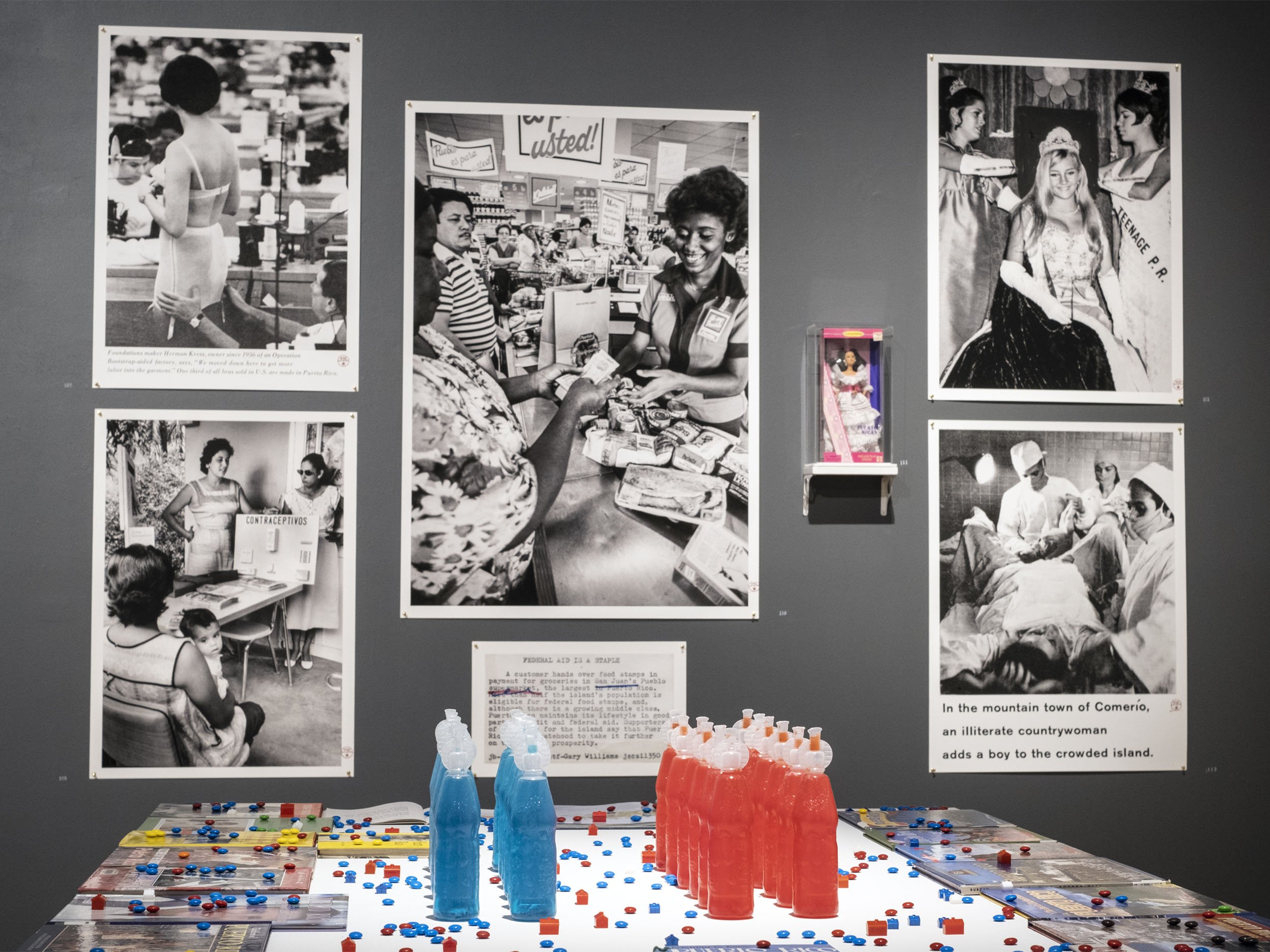  Installation view (cropped).  Schoolbooks and Kool-Aid  (detail in foreground); beauty and birth-control industry-related photographs, objects, and captions. Clockwise from circa 1960, 1964, 1980, circa 1996, 1968, and 1961 | 2019-2021.  The Museum 