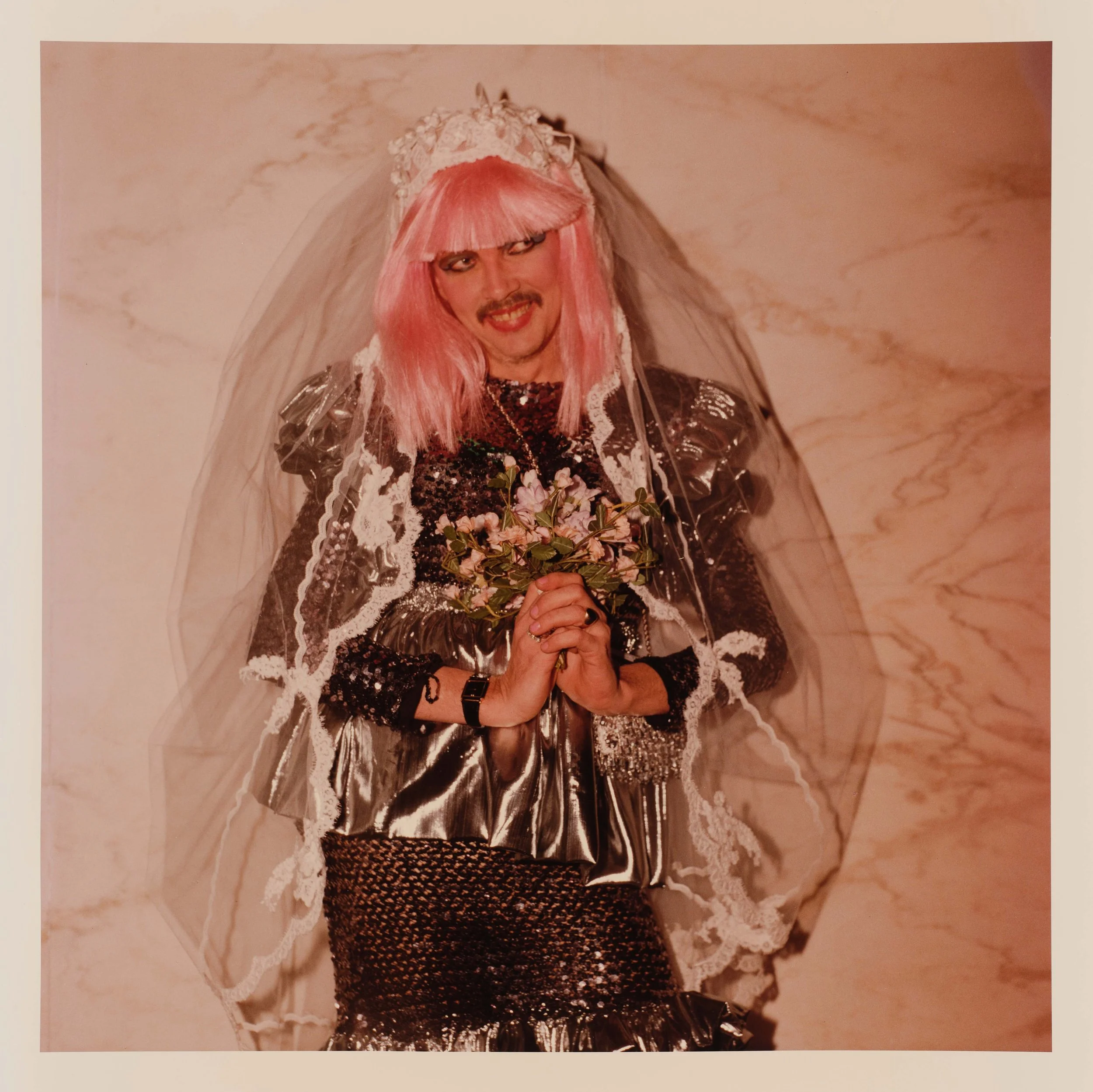 a peron with pink hair, metallic top, and sheer veil with hands clasped