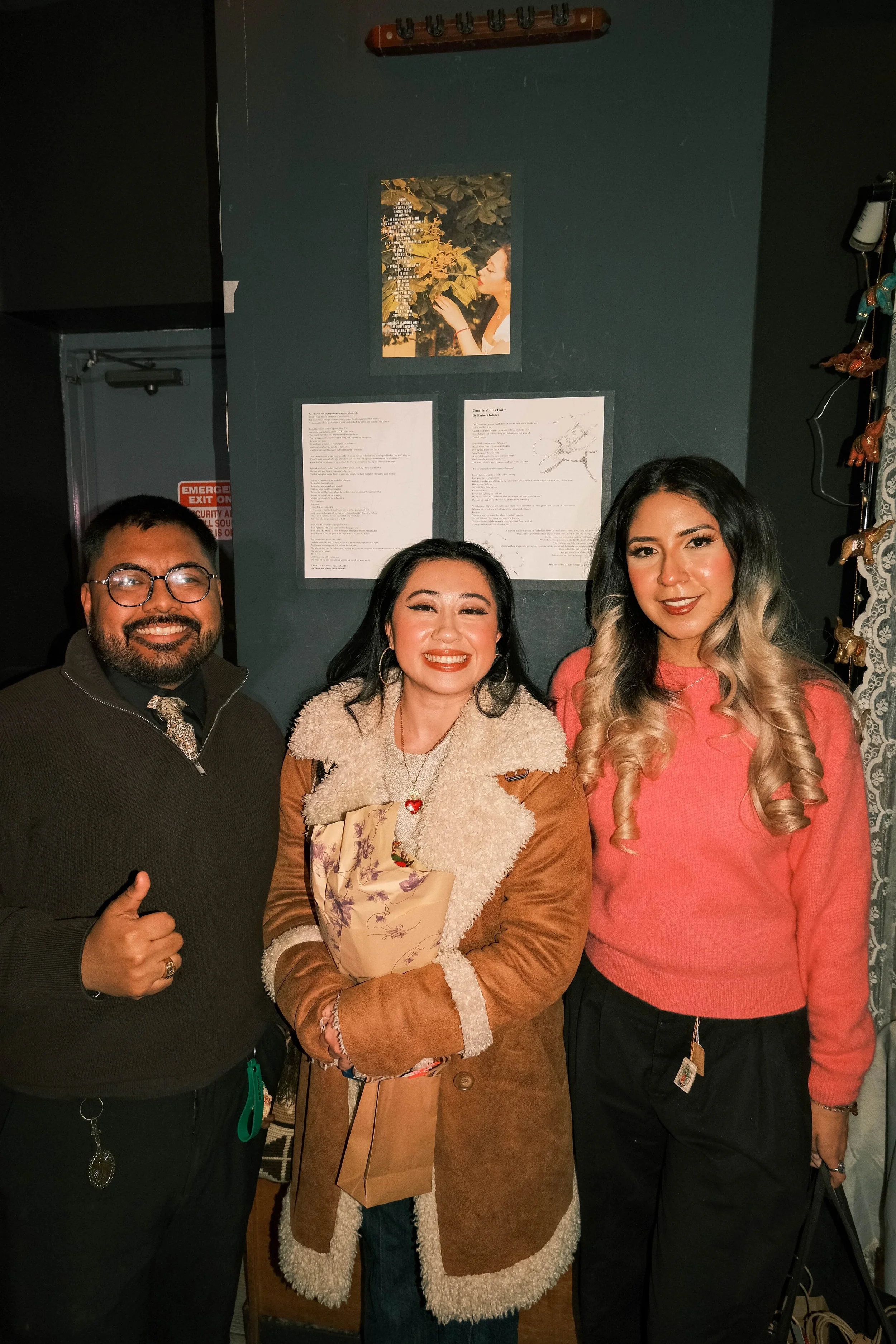 Three people stand in front of a wall of poems at a Con Tiempo event