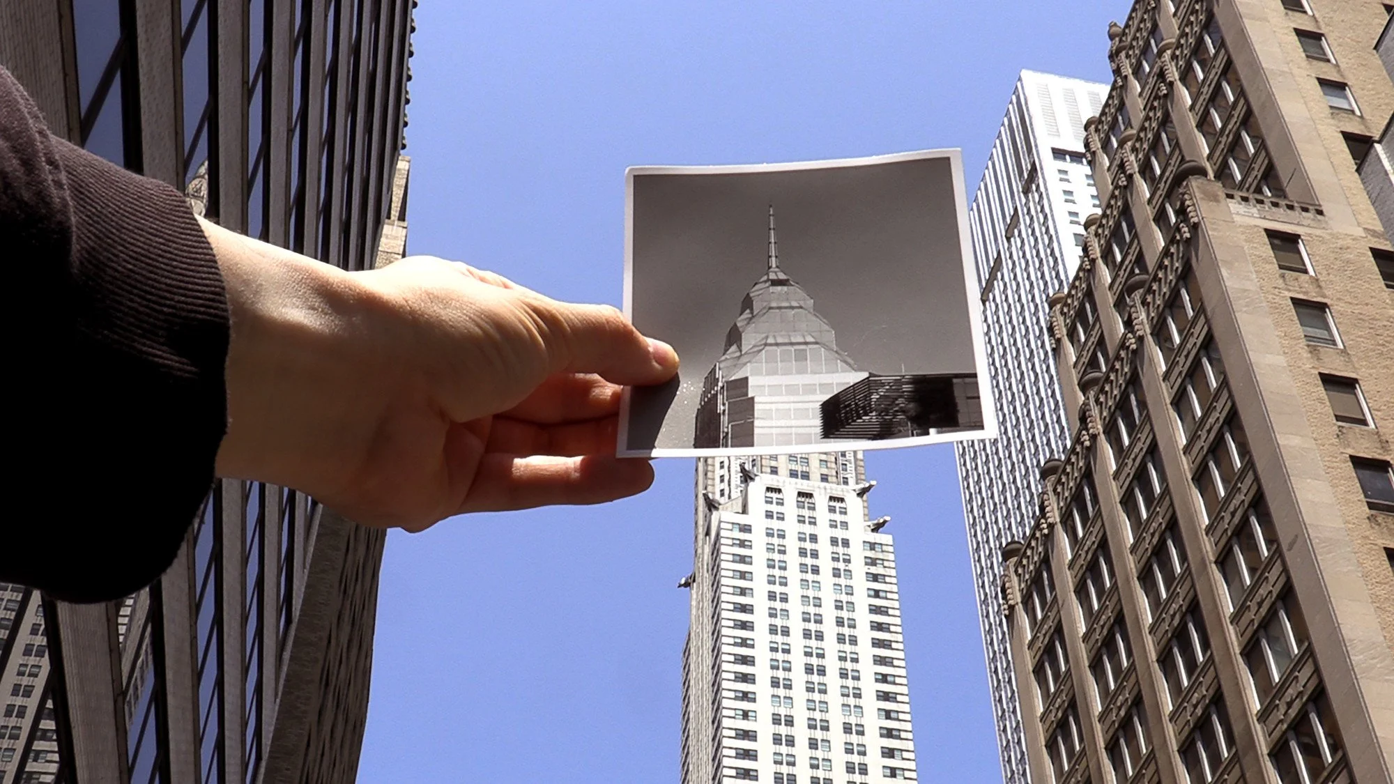 A person holding a photo of a Manhattan skyscraper in front of a skyscraper