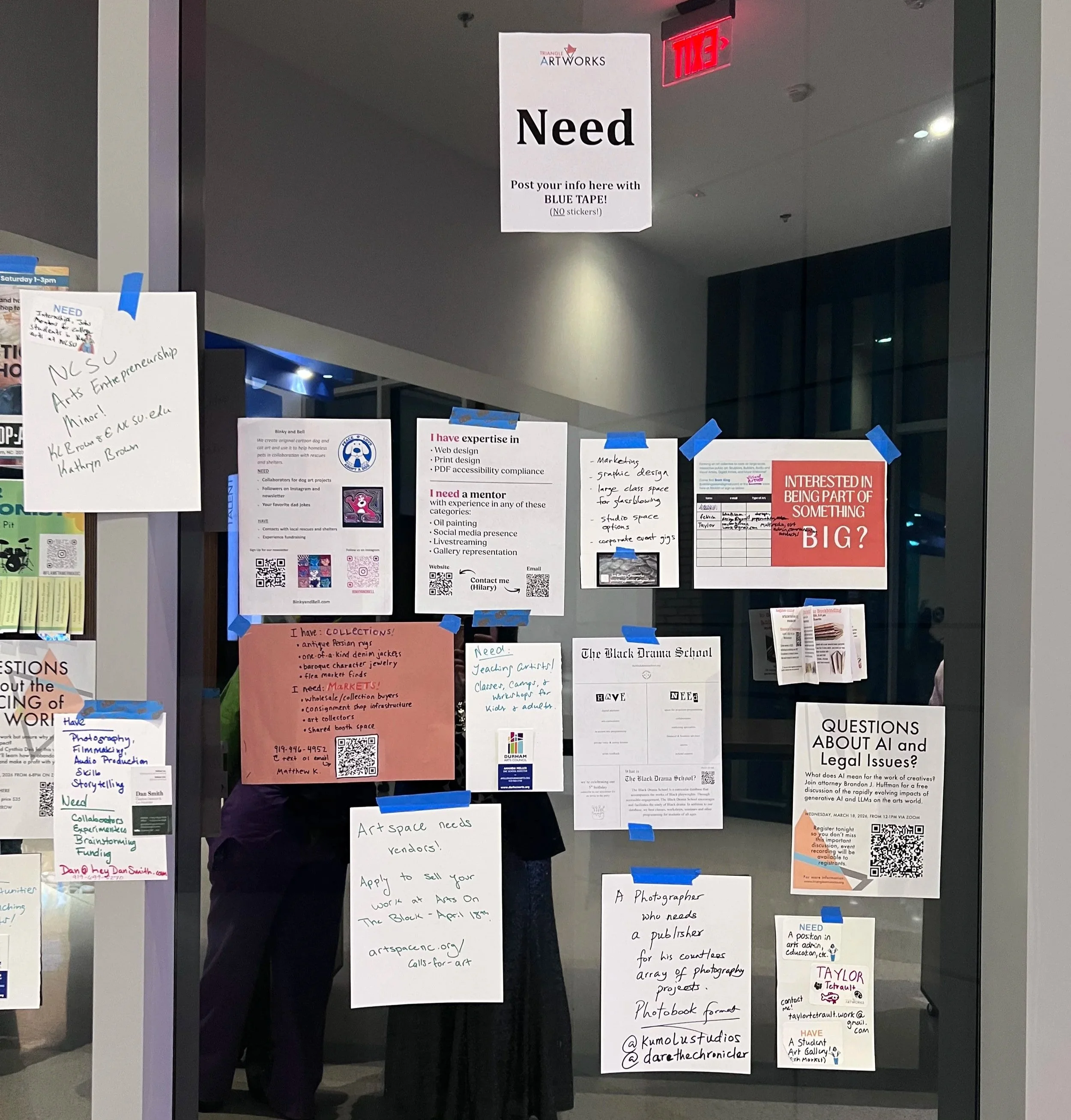 An image of a glass wall with many pieces of paper, printed with requests or offers for studio space, support, jobs, gigs, work and grants for artists and performers taken at SMASH! 2026 in North Carolina