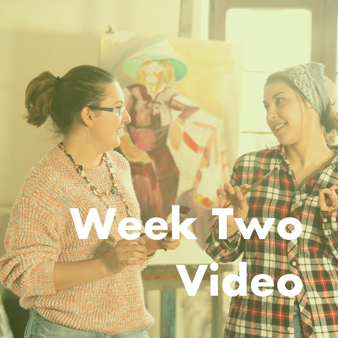 Two women hold paintbrushes and talk about their artwork, they are white and the one on the left has glasses and a ponytail, the one on the right wears a plaid shirt.