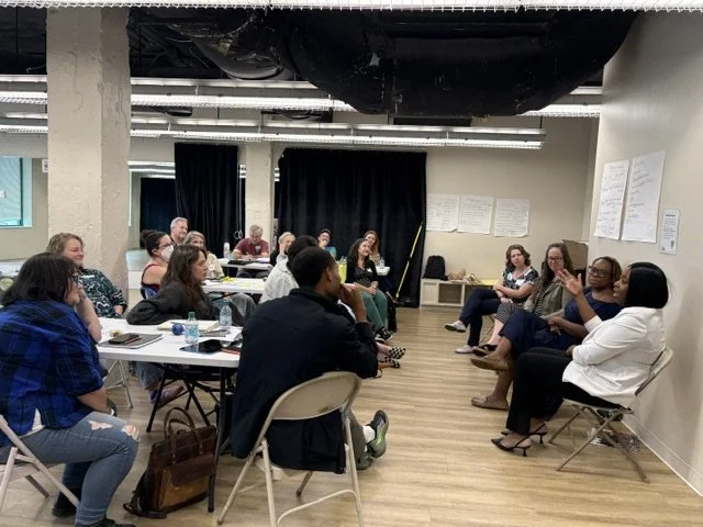 15 members of the 2027 ArtsCore Cohort are seated and listening to 4 arts leaders, seated before them.