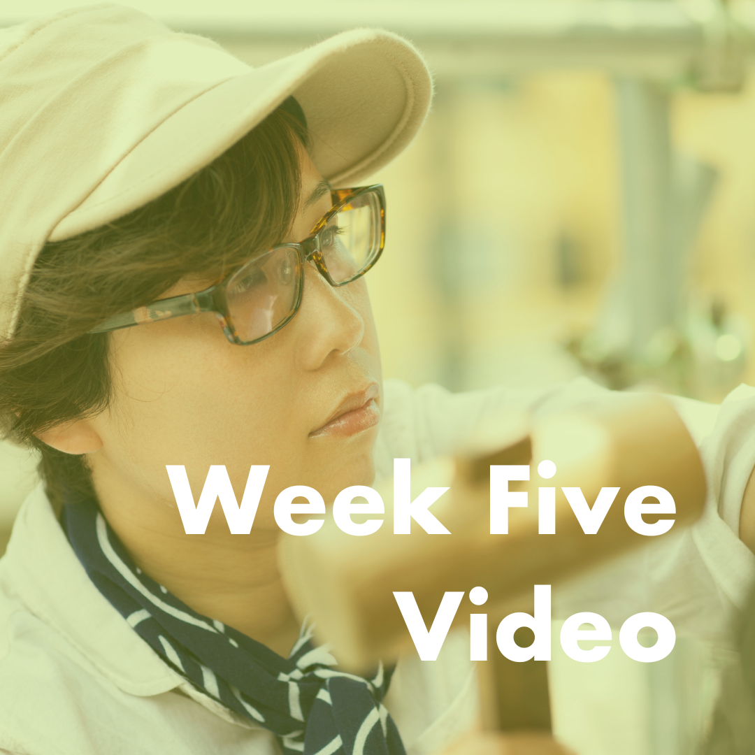 young asian woman in glasses wearing a tan cap is using a wooden mallet to hit a sculpture