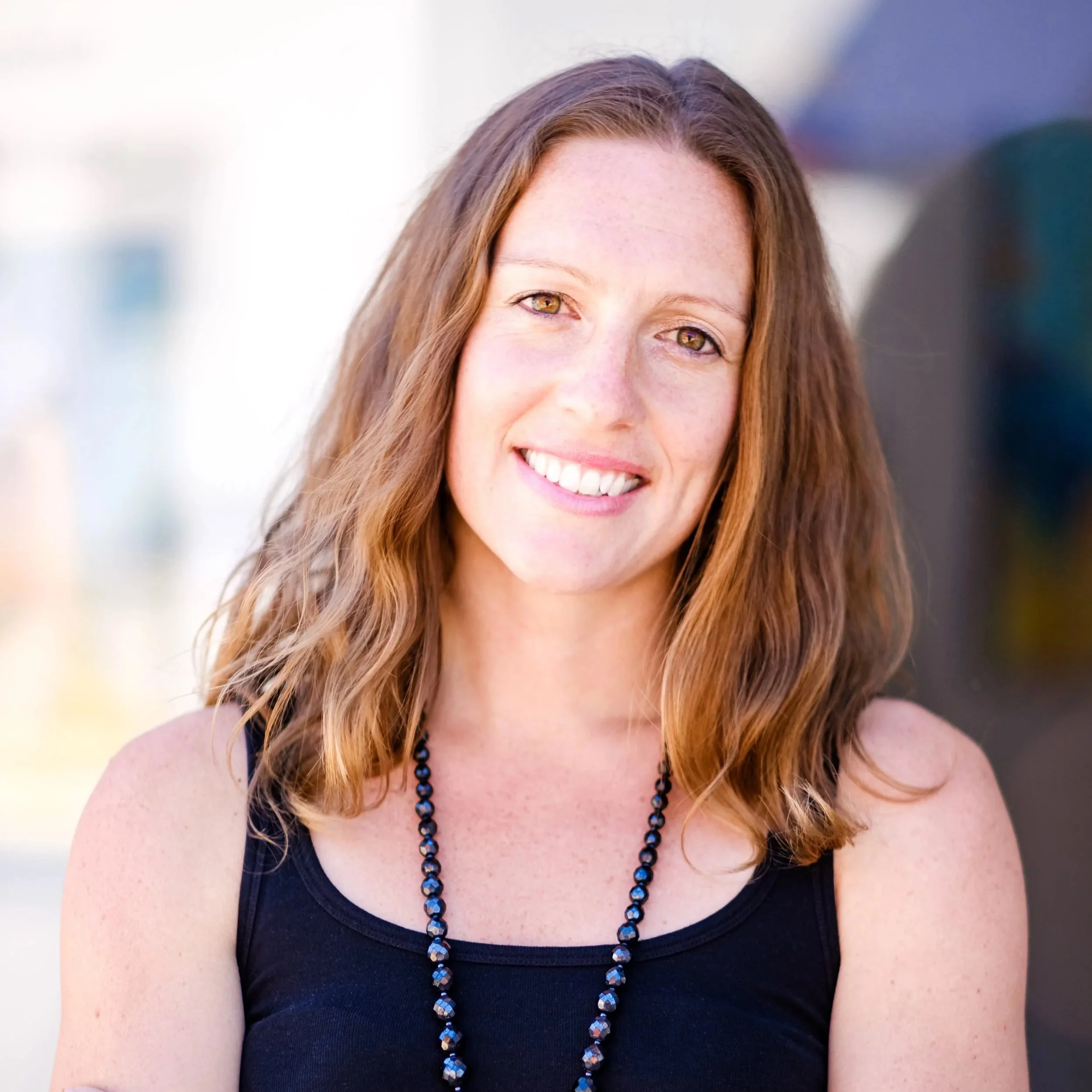 Katie is a pale-skinned woman with wavy dark blonde hair and she is smiling at the camera