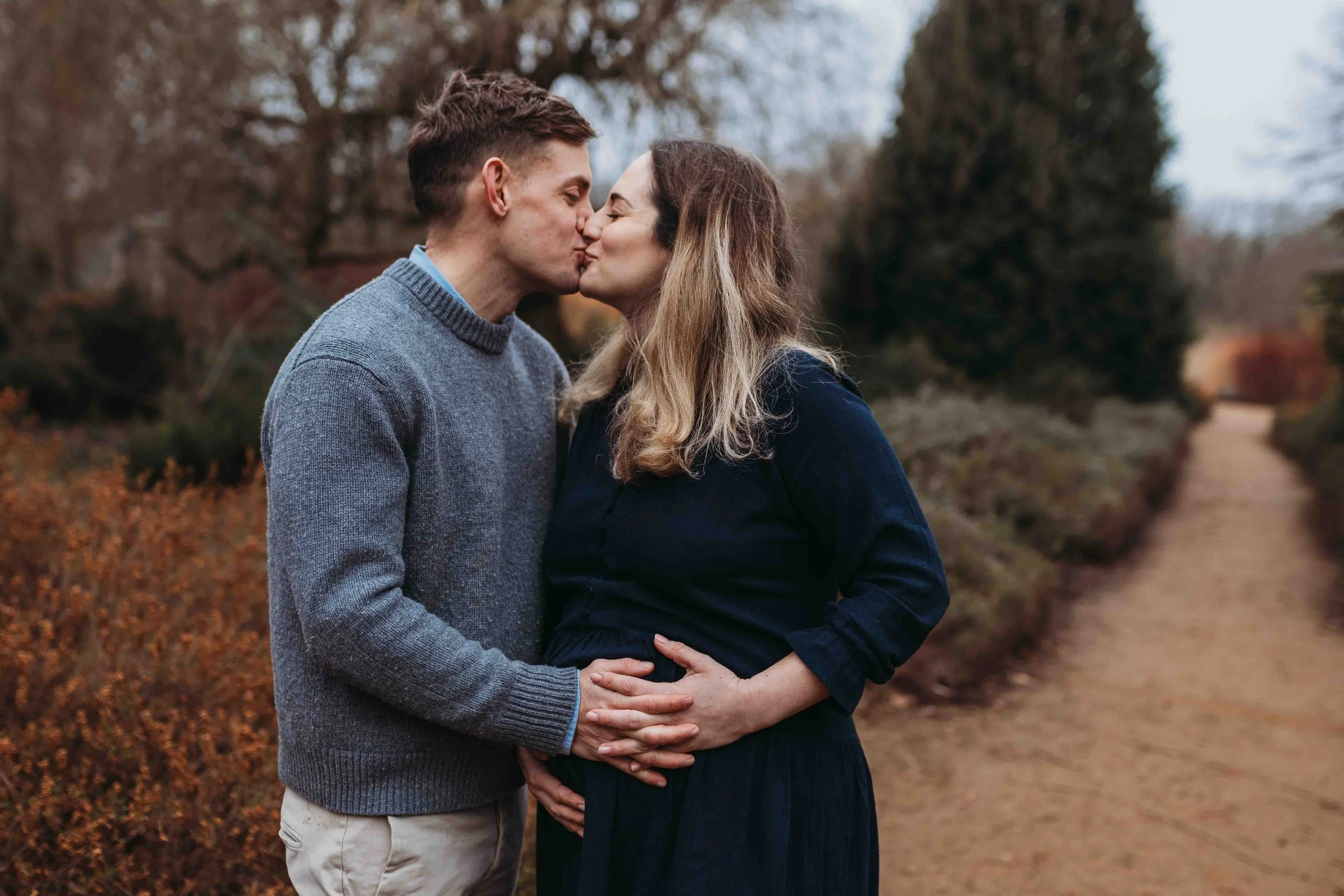 An expecting couple kissing and holding bump in Richmond Park at maternity session