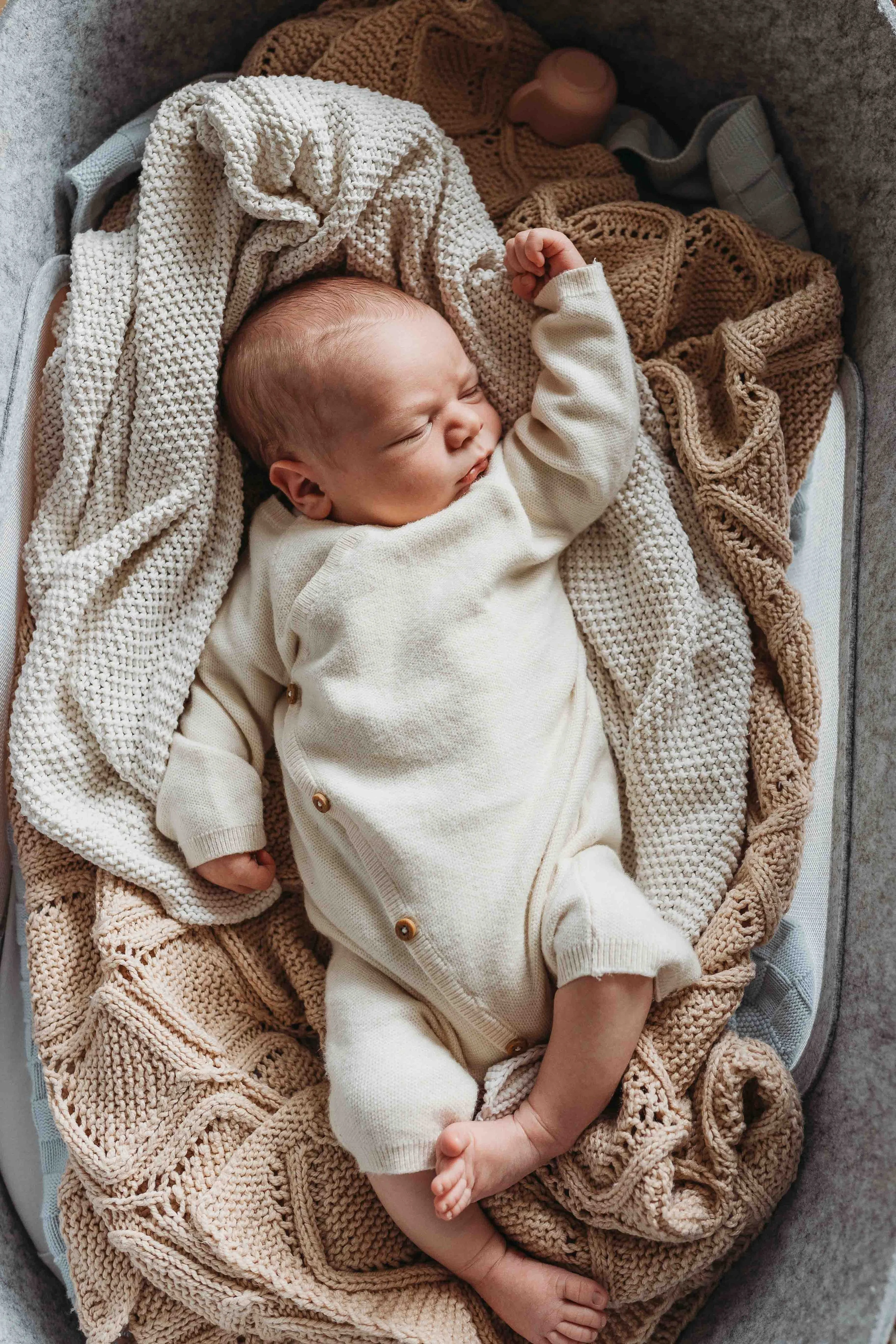 newborn baby sleeping in cream knit outfit wrapped in soft blankets during an at-home newborn session in London
