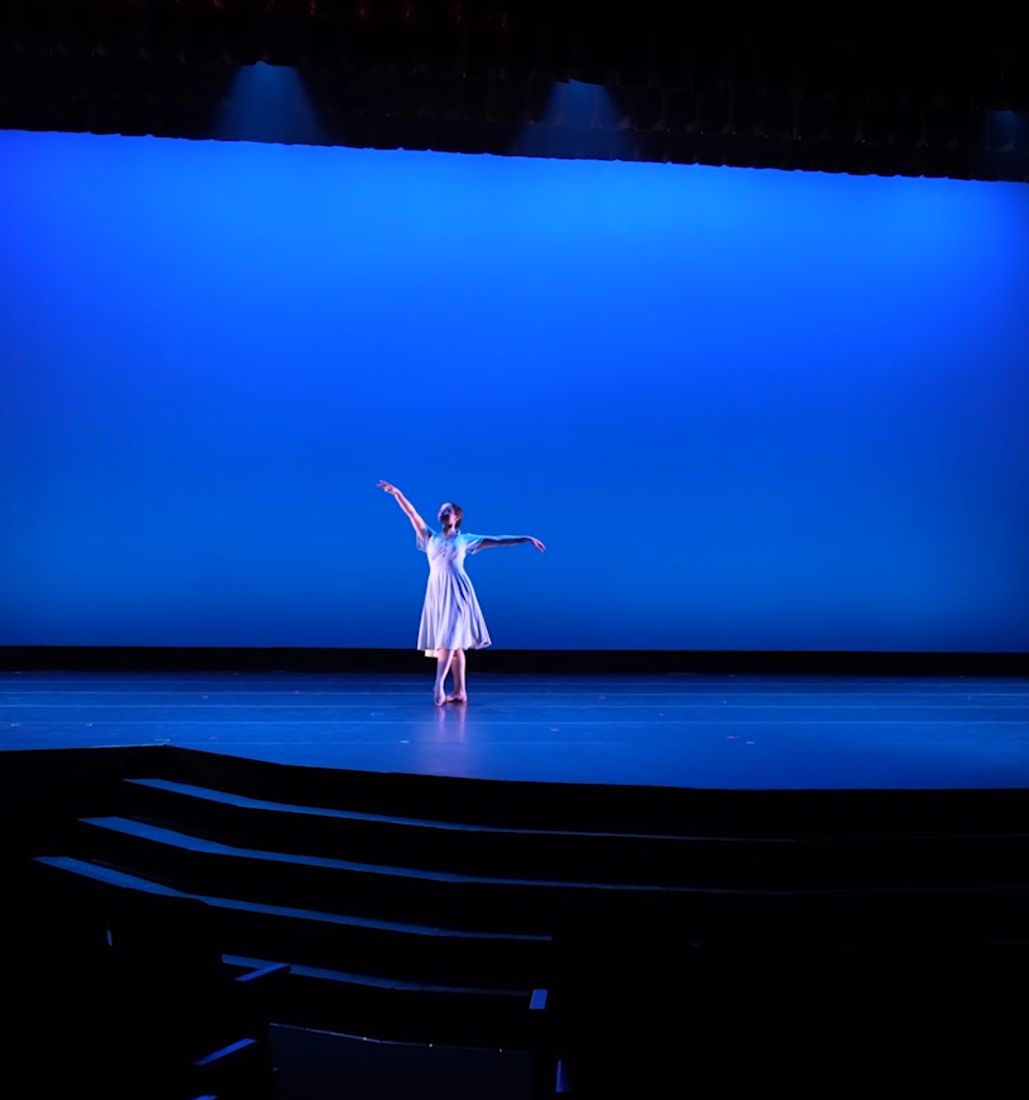 Solo dancer on large stage, In white dress that's flowing, Blue Background,