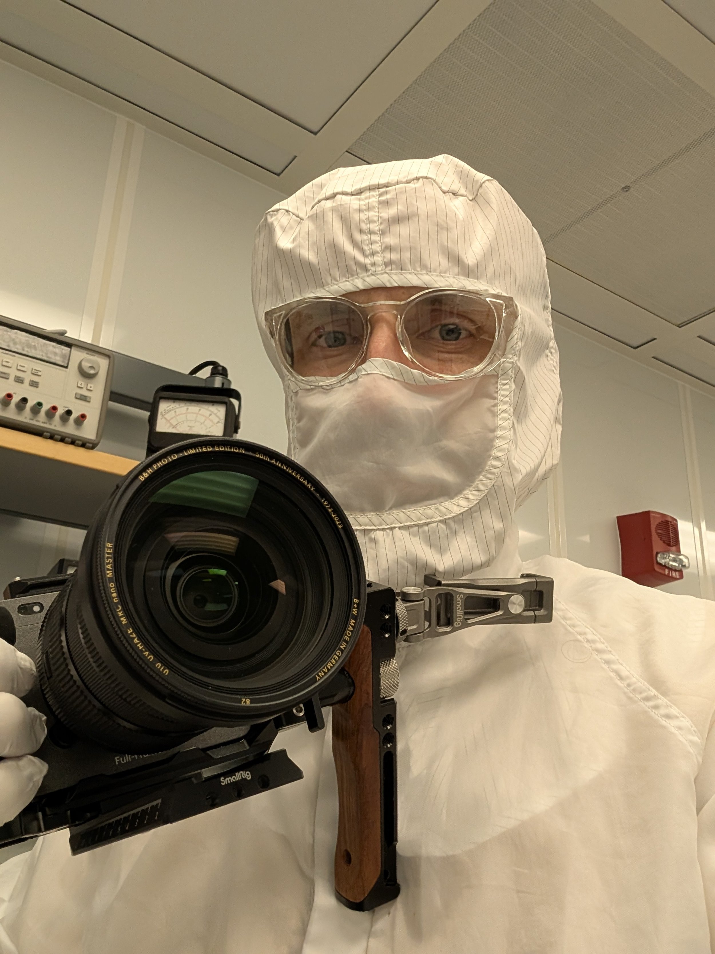 Man in clean room safety gear, holding camera in hand, man is looking into camera taking a selfie.