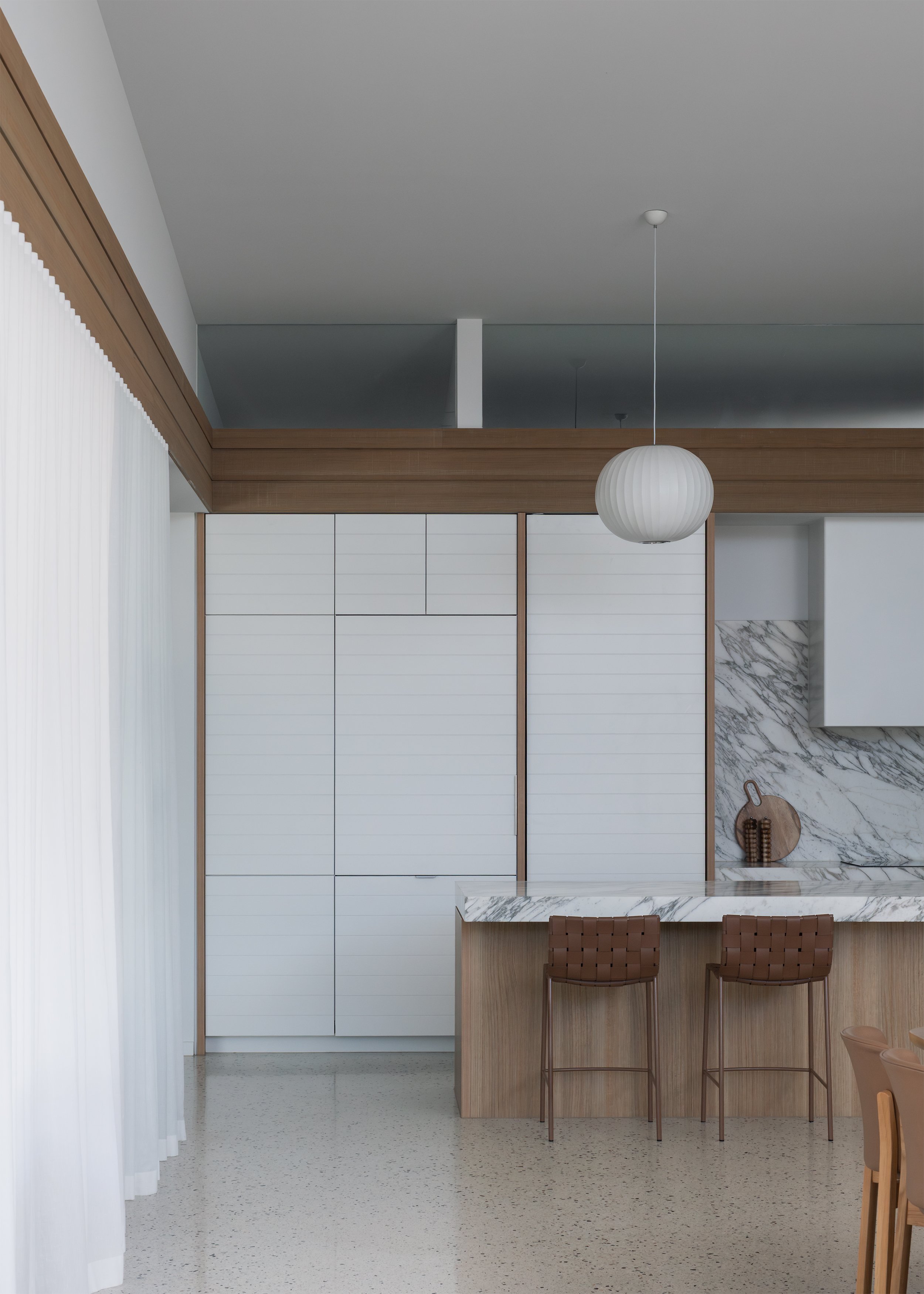 Kitchen and dining area with timber joinery, white cabinetry and marble surfaces beneath the continuous timber datum.