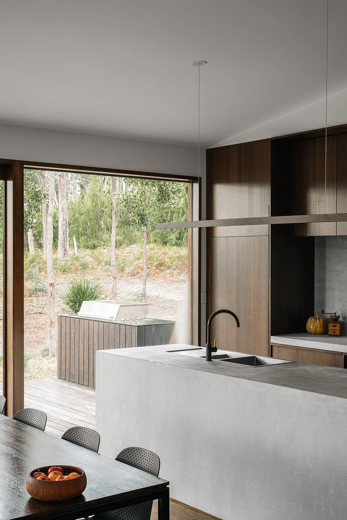 Kitchen at Killora Bay featuring a concrete island, dark timber cabinetry and sliding doors connecting to the bushland deck.