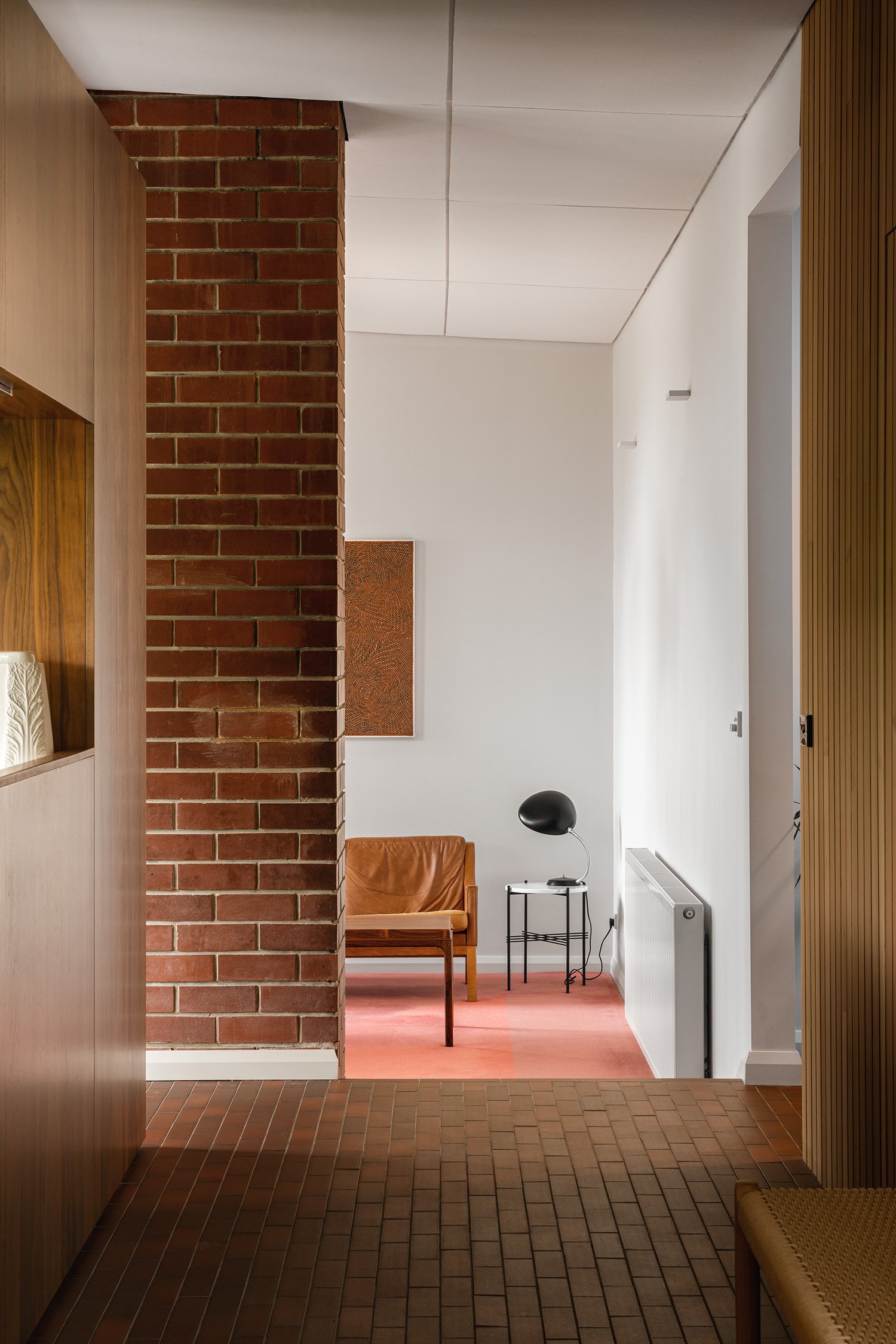 Red brick and timber frame a view to a leather armchair and pink carpet in a mid century home in Melbourne's bayside suburb of  Frankston South