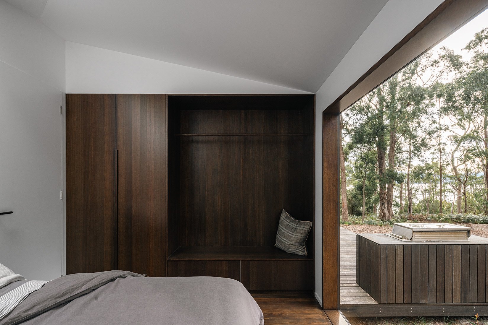 Main bedroom in Killora Bay, architect Lara Maeseele’s own Bruny Island home, with dark timber joinery and views into the bush.