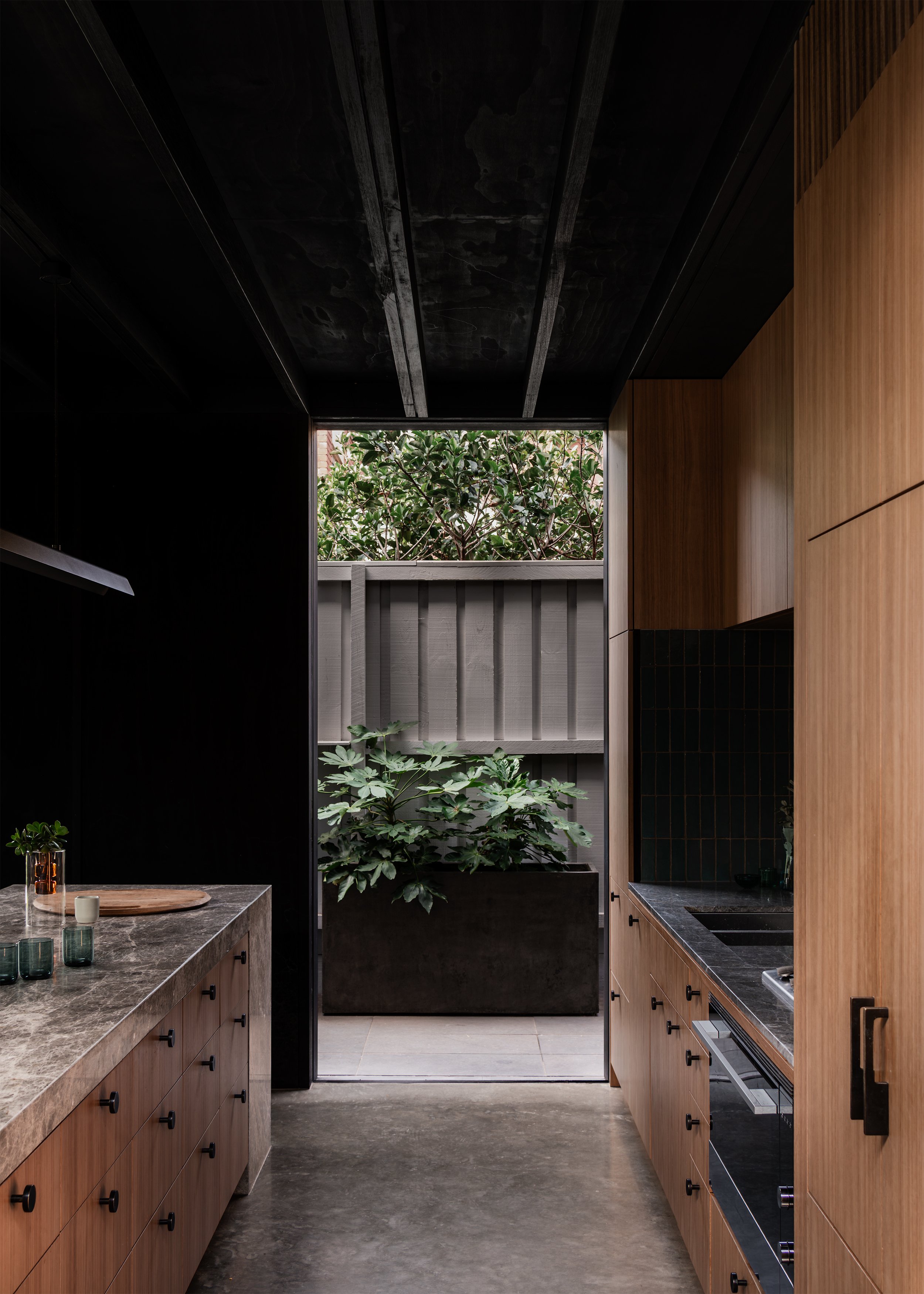 Galley kitchen opening to a planted side courtyard, extending garden views into the interior.