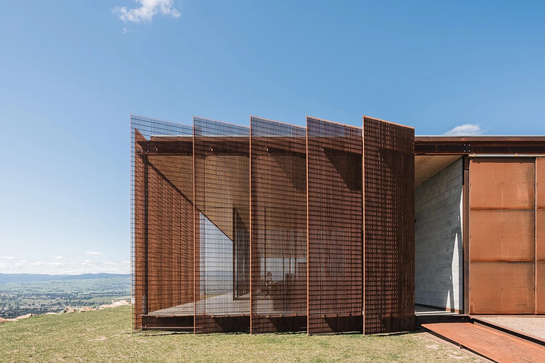 Operable weathered-steel screens shade the glazed living volume of Mansfield House while maintaining views across the valley.