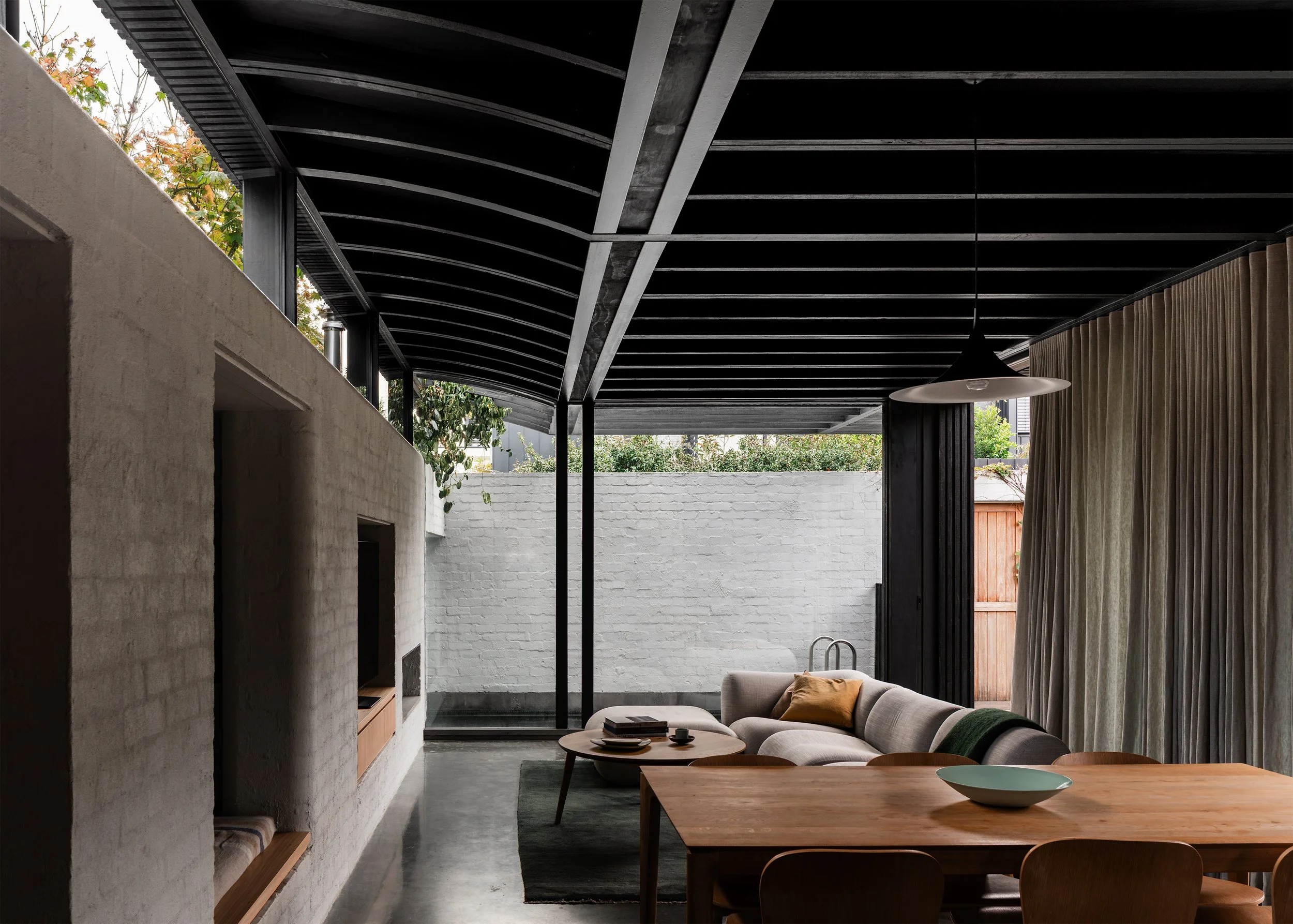 Open-plan dining and living space beneath the dark timber roof, framed by garden walls and glazing.