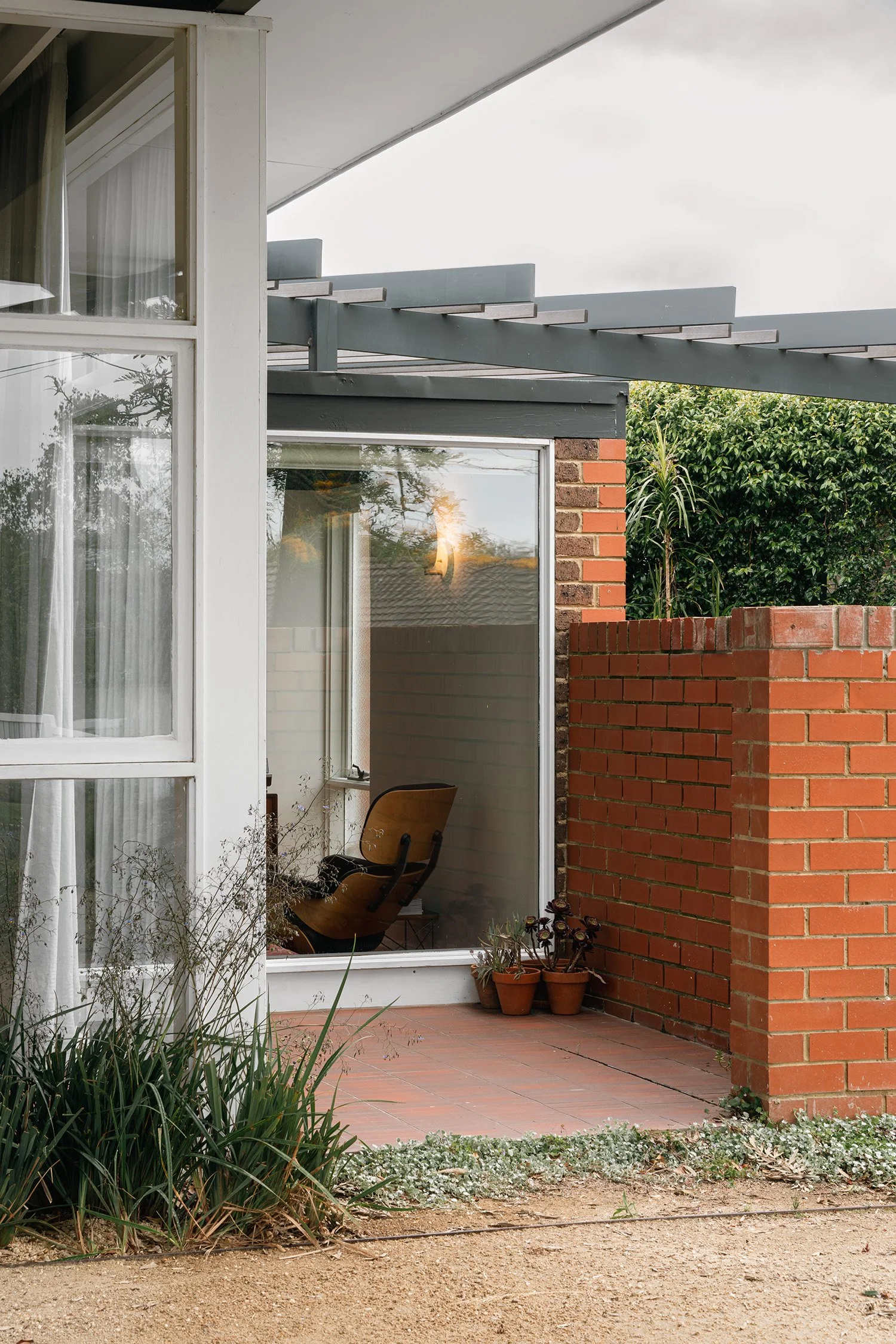 Brick-walled patio beside full-height living room windows and a pergola at the Frankston mid century modern house.