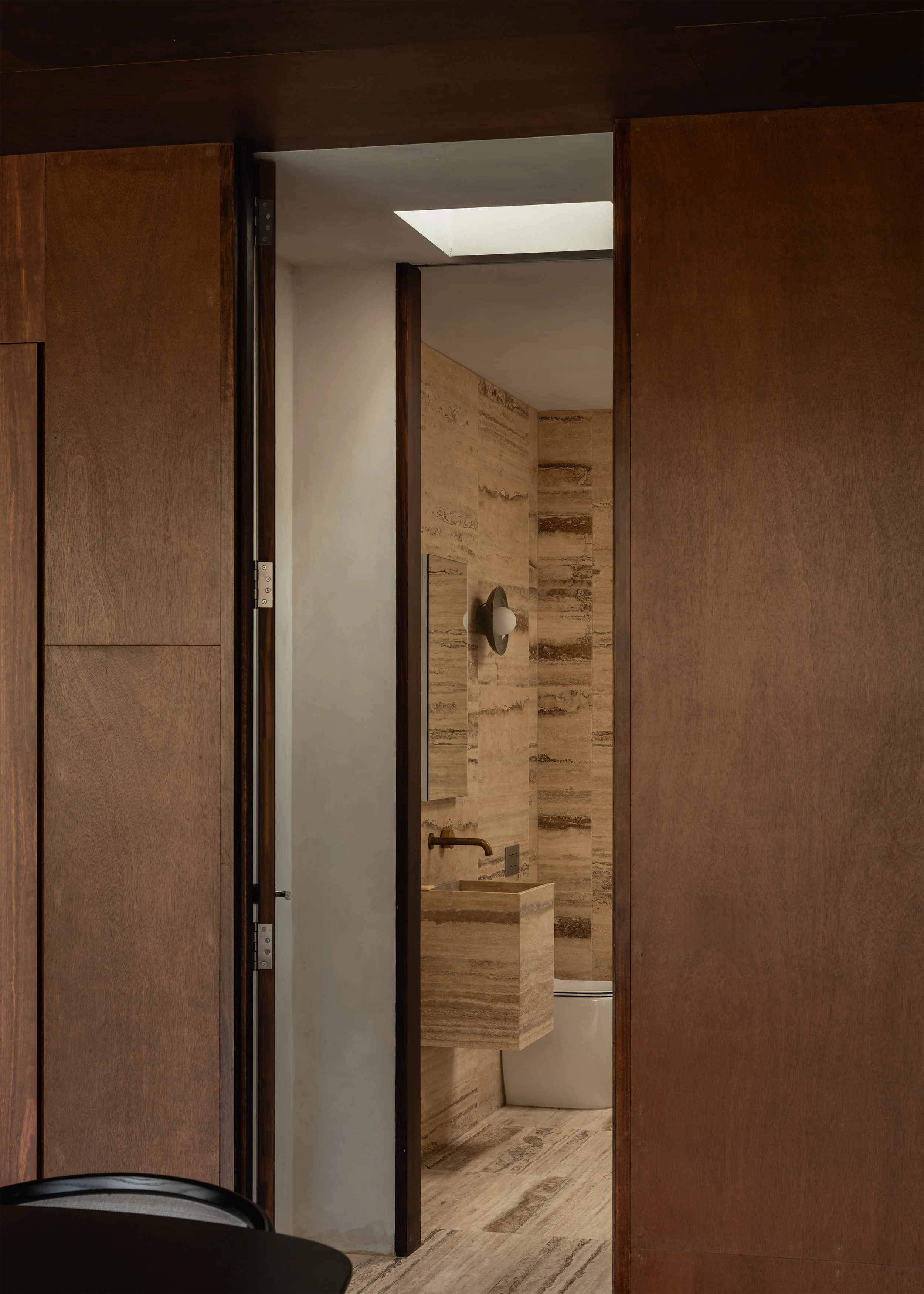 Bathroom viewed through dark timber joinery, with travertine tiles.