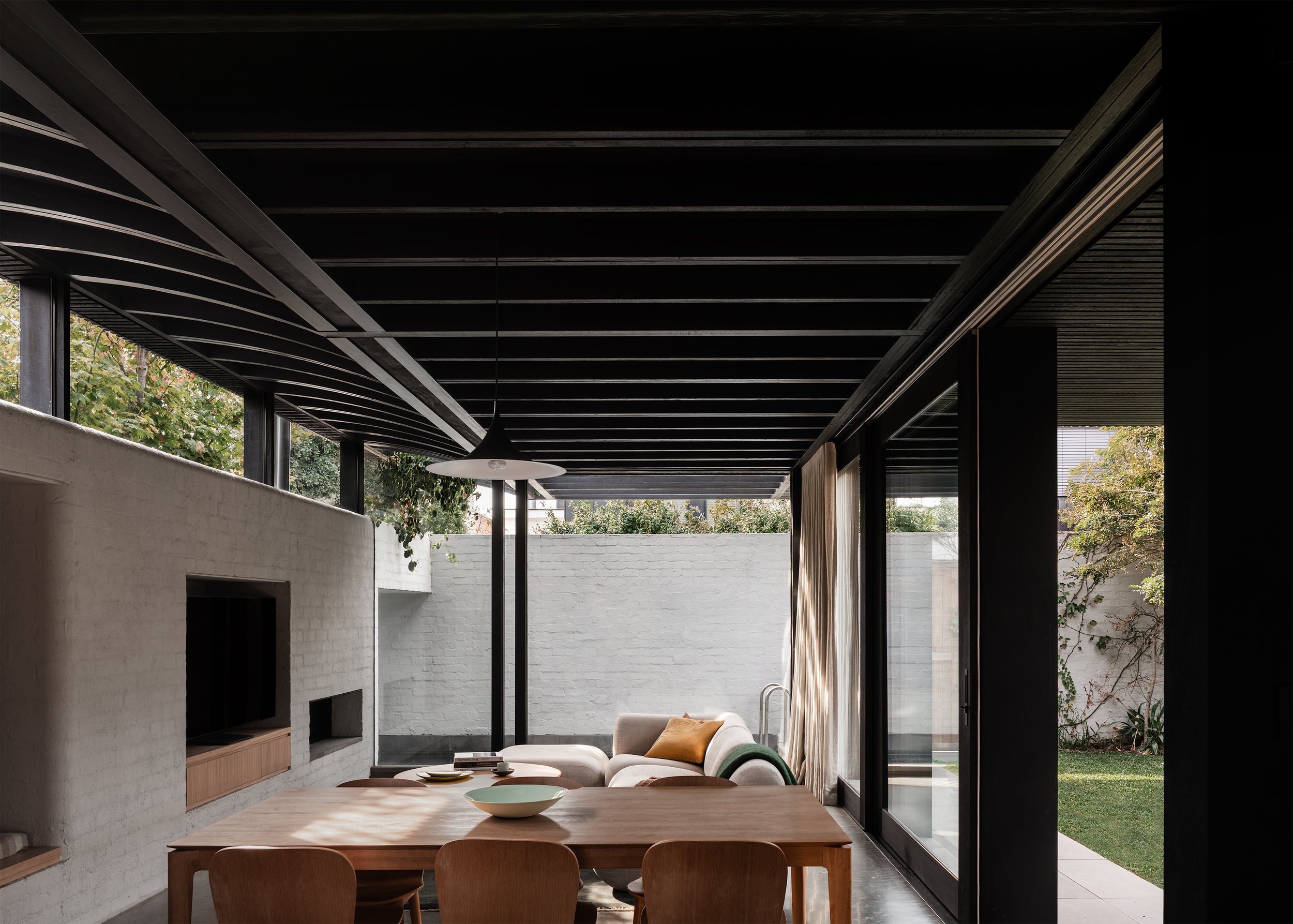 Open-plan dining and living space surrounded by glazing, garden and pool at Borrowed Garden House in Albert Park.