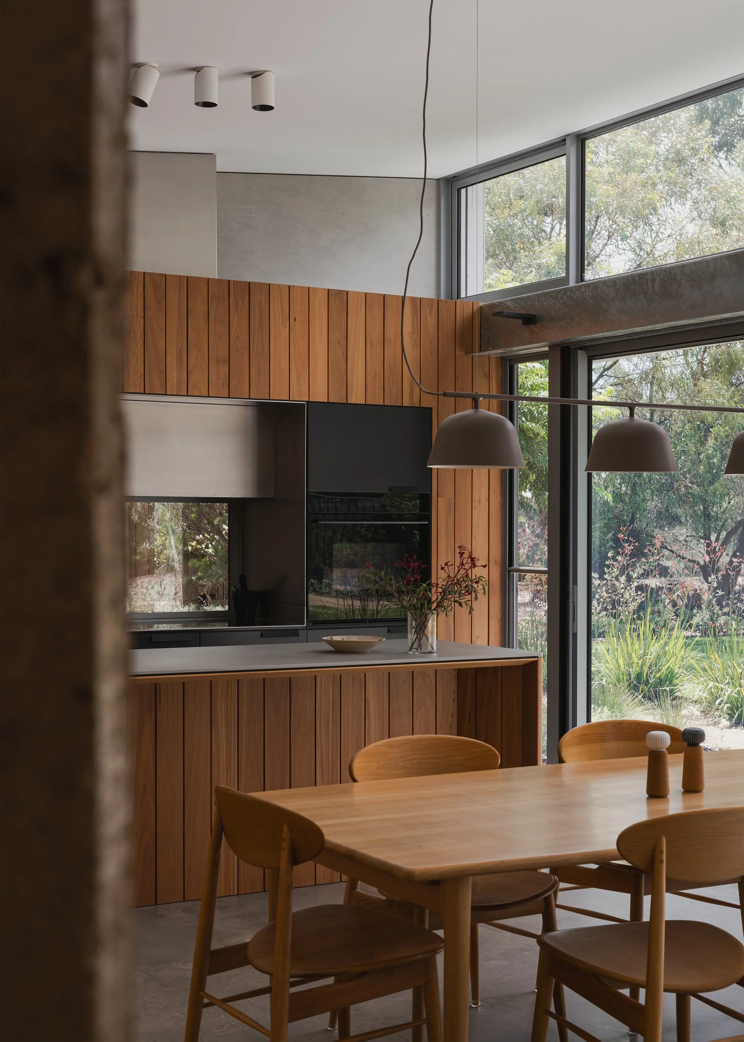 Timber kitchen island and dining furniture at Forest Road House, with pendant lighting and tall windows framing the garden.