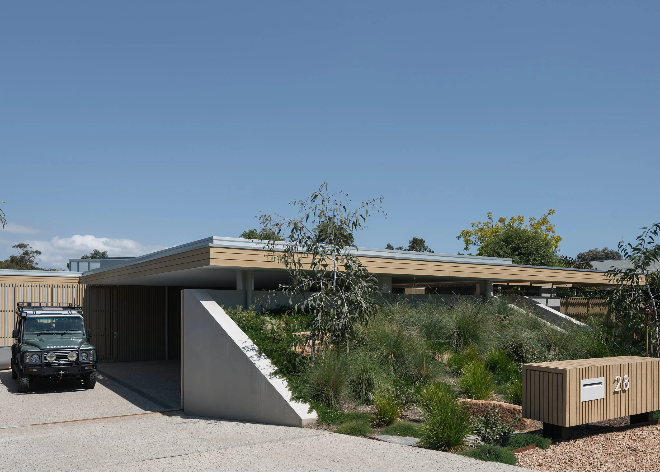 Street frontage of Channel by Megowan Architectural, with a planted berm, low roofline and sheltered carport in Mornington with Defender.