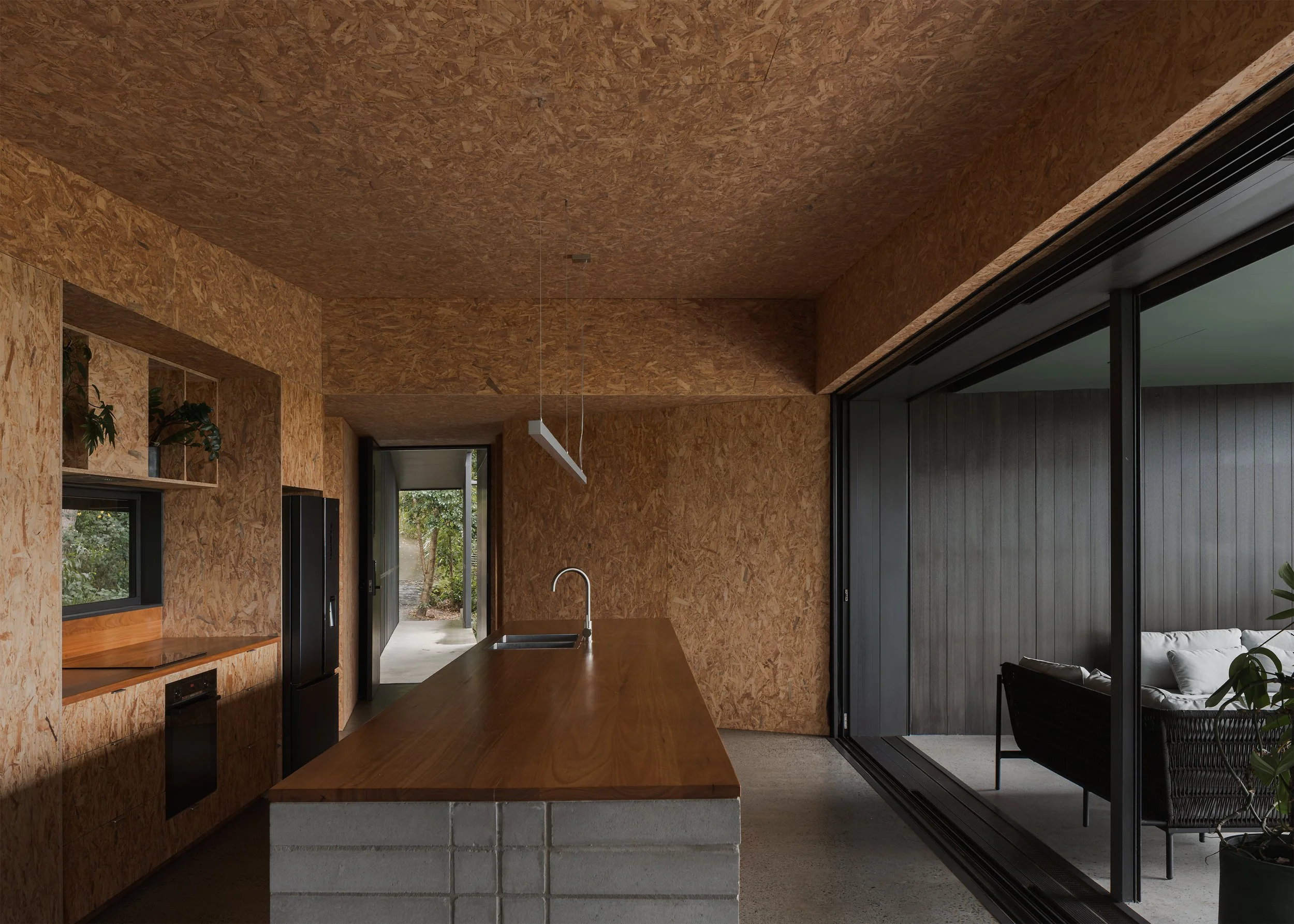 OSB-lined kitchen at Tallowwood Cabin opening through sliding glass doors to a covered deck overlooking the Gold Coast hinterland.
