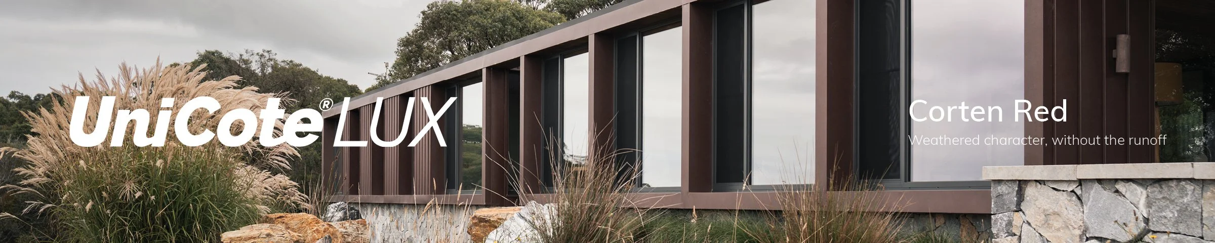 Close exterior view of Horizon House by Neil Architecture, showing UniCote LUX Corten Red cladding, a stone base and ornamental grasses.