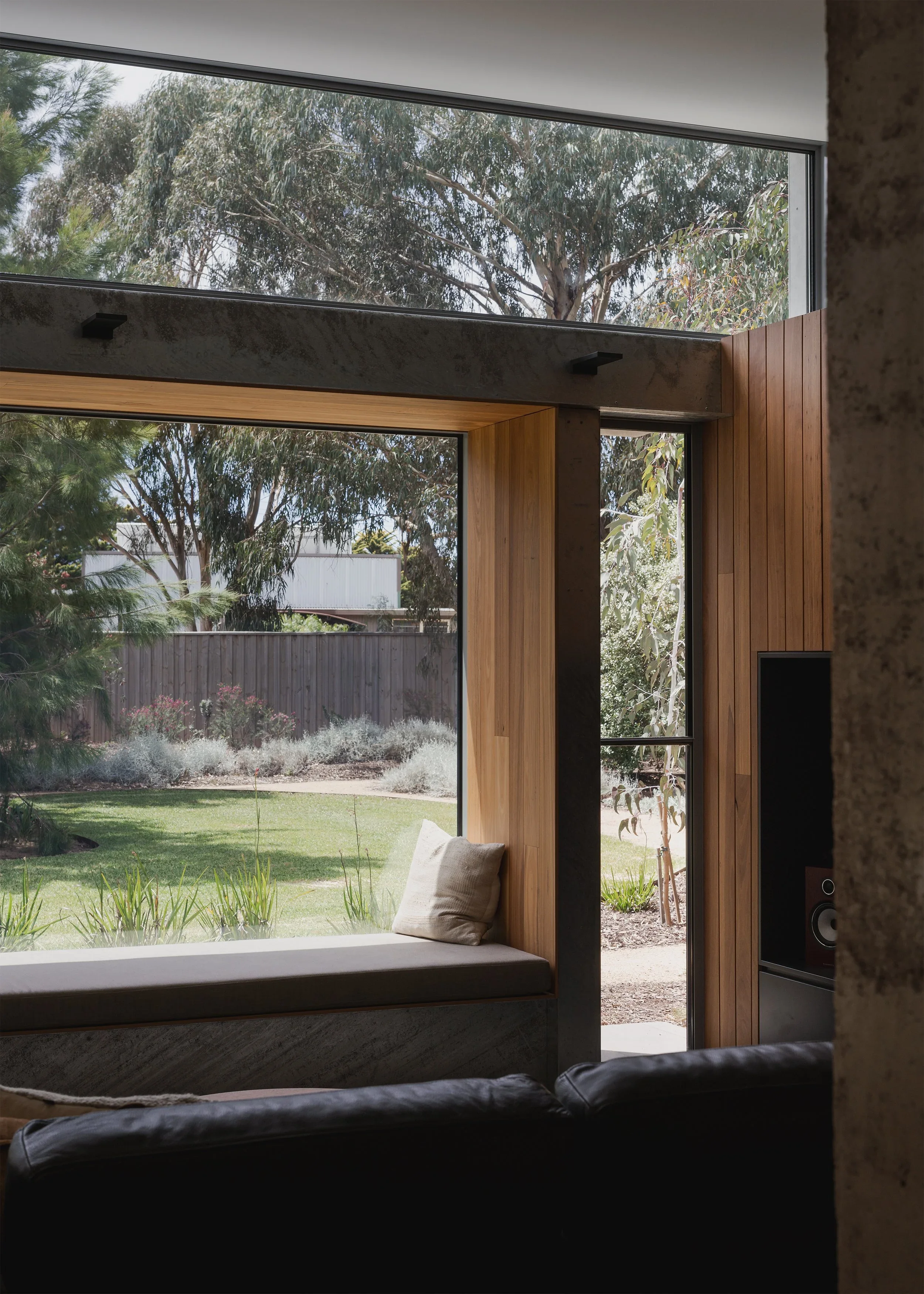 Cushioned window seat framed in timber and exposed steel at Forest Road House, overlooking lawn and gum trees.