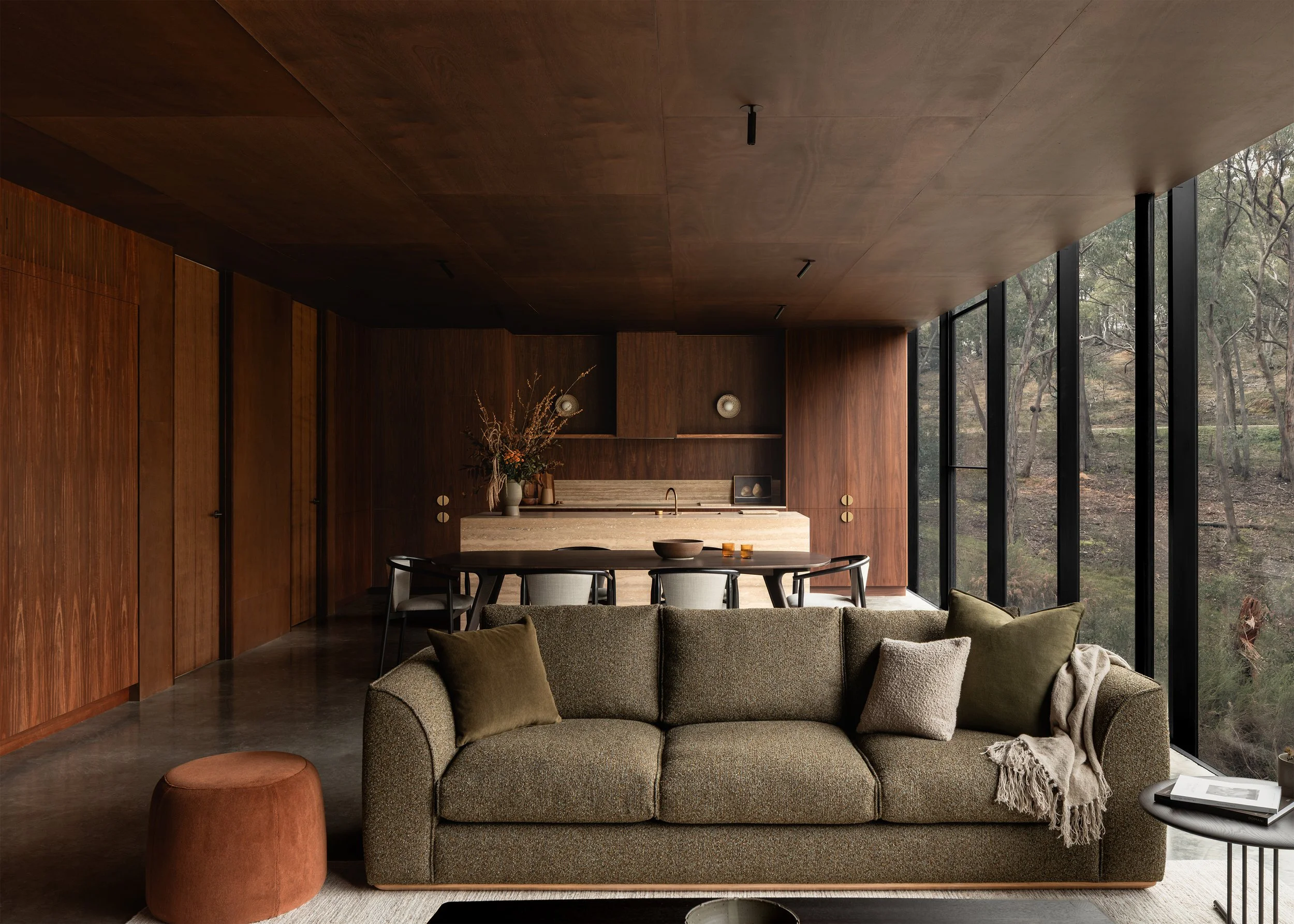 Compact open-plan living, dining and kitchen space with Cosh Living and Kett Furniture extending alongside full-height bushland glazing at Matchbox.