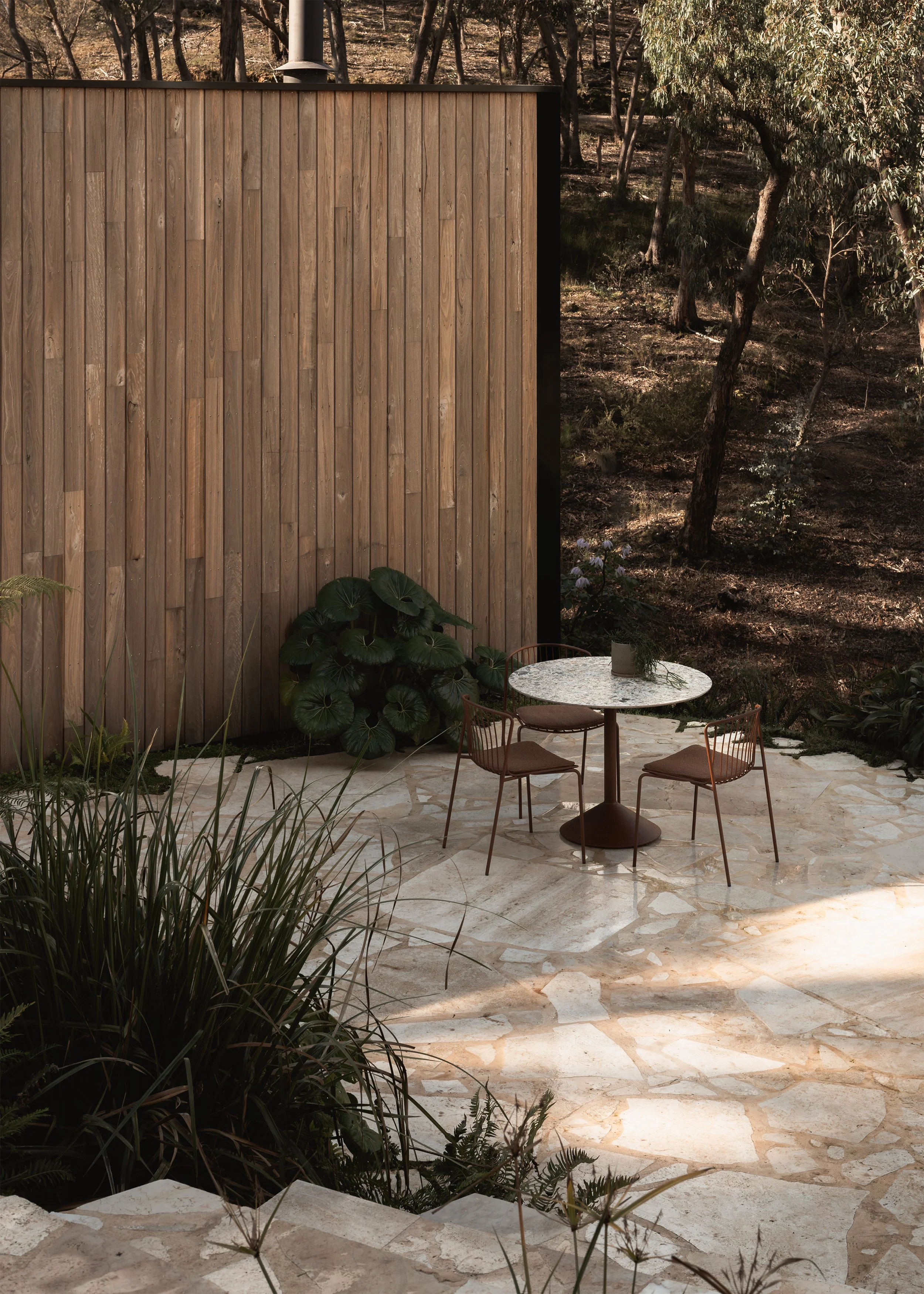Stone-paved outdoor terrace at Matchbox with dining setting, native planting and the timber-clad exterior wall.