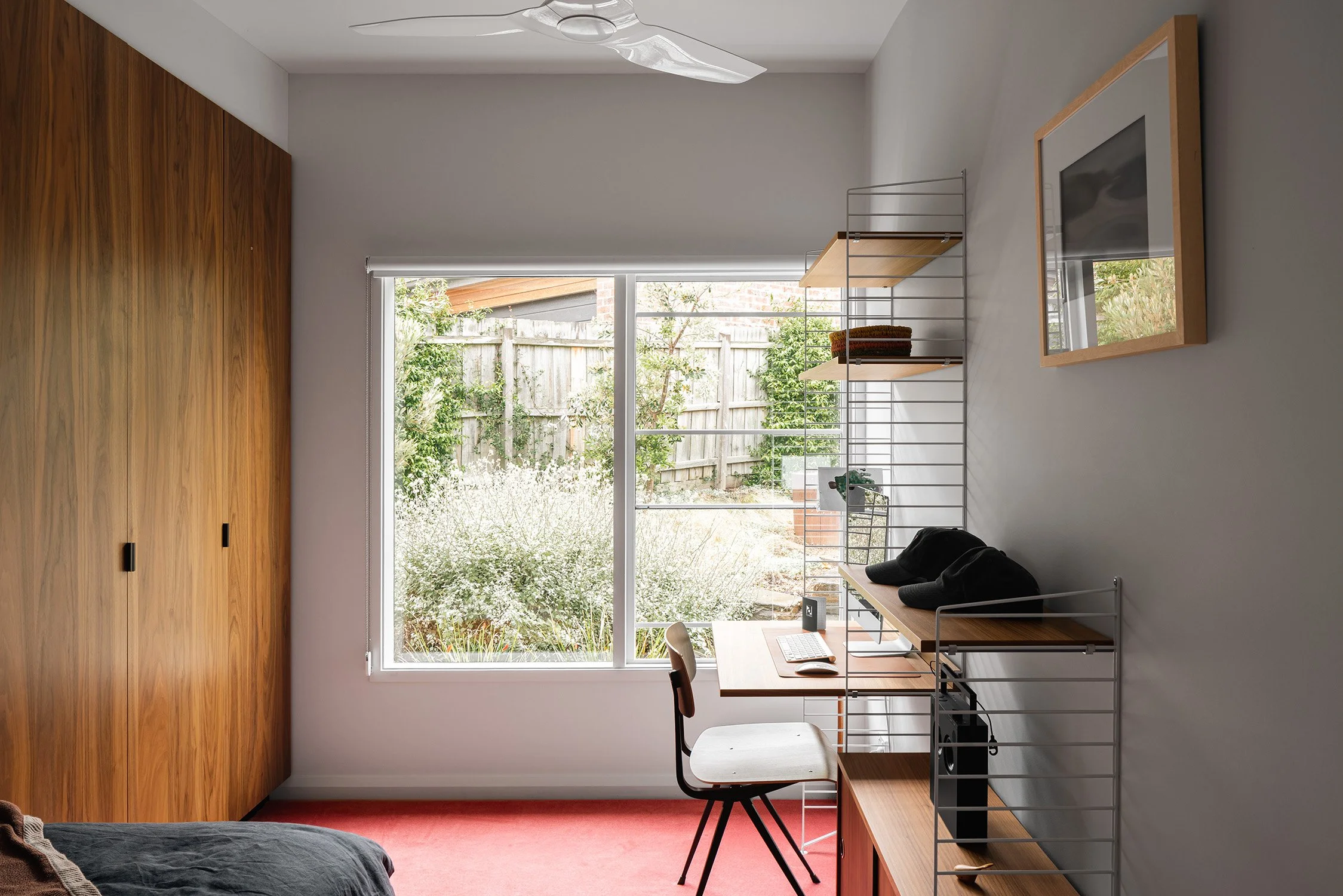 Bedroom with workspace in a mid century home in Melbourne, Australia, with a wall-mounted desk, timber wardrobes and a large garden window.