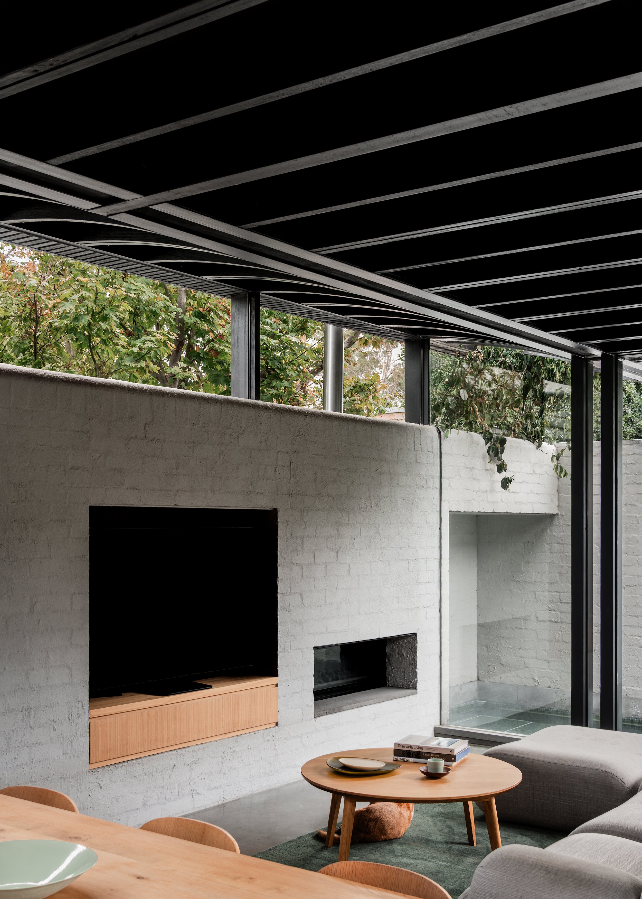 Living area with built-in joinery, pool edge and neighbouring tree canopy visible above the garden wall.