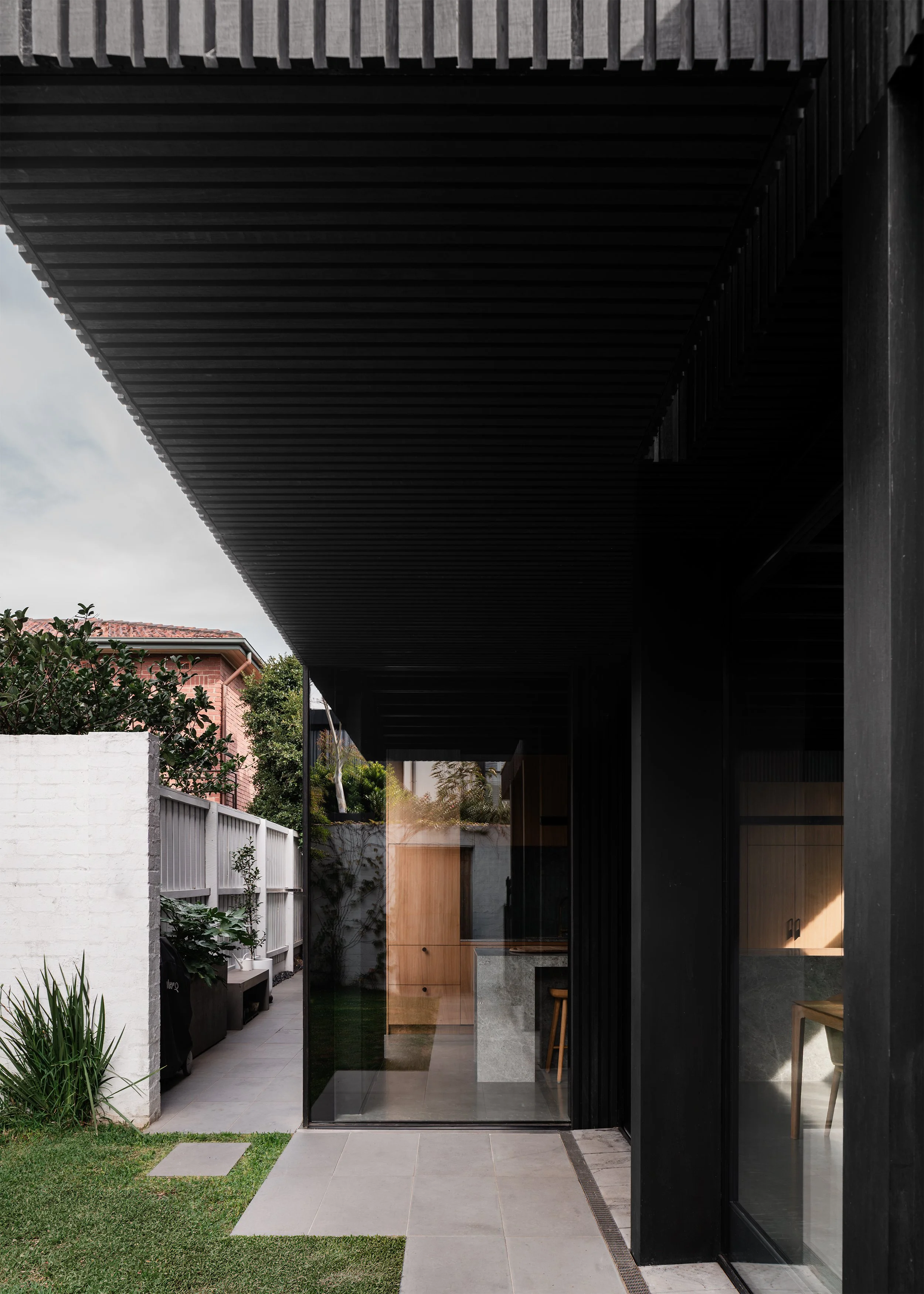 Garden elevation of Borrowed Garden House with black timber cladding, deep eaves and full-height glazing.