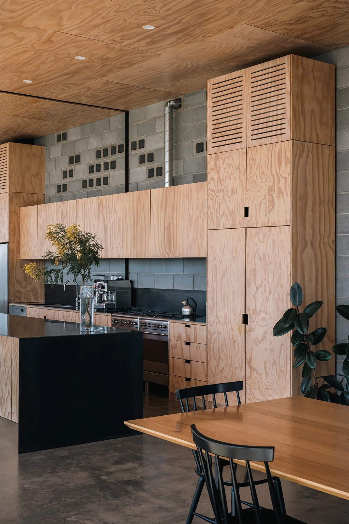 Minimalist plywood kitchen with a black steel island and exposed concrete blockwork in Robbie J Walker’s Mansfield House.