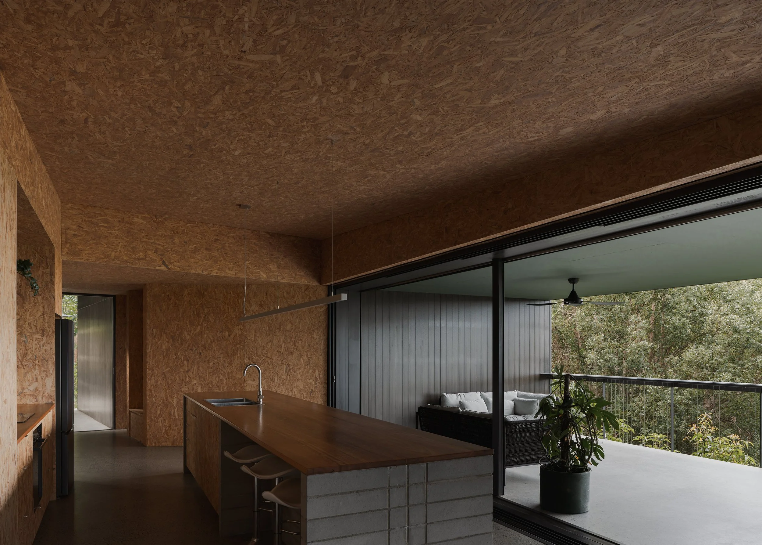 Open-plan kitchen and covered deck at Tallowwood Cabin express Australian simplicity through a restrained palette of OSB, timber and concrete.