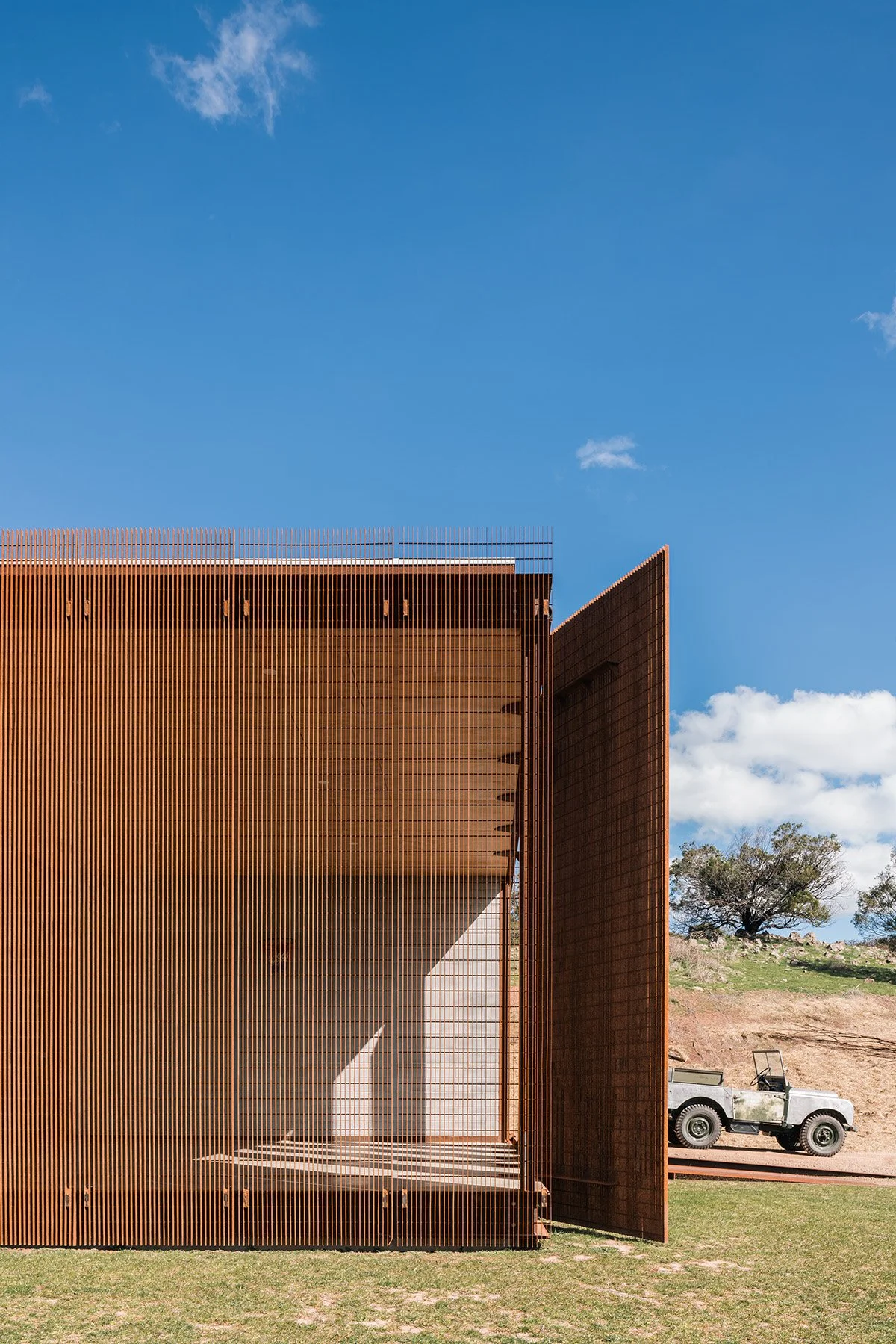Weathered-steel mesh screens wrap the glazed end of Robbie J Walker’s minimalist rural home in Mansfield.