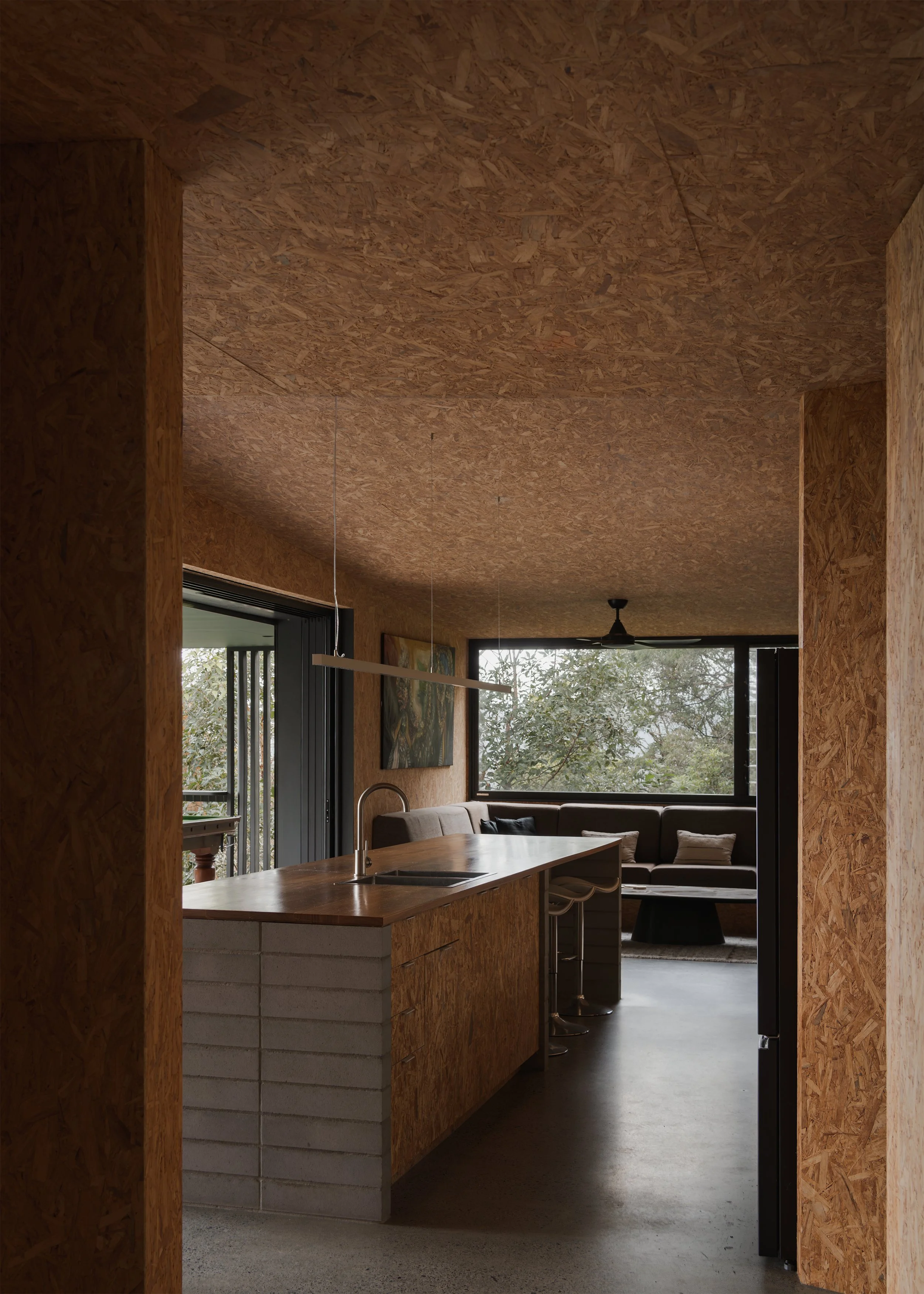 Internal passage at Tallowwood Cabin framing the kitchen island, built-in living area and surrounding bushland beyond.