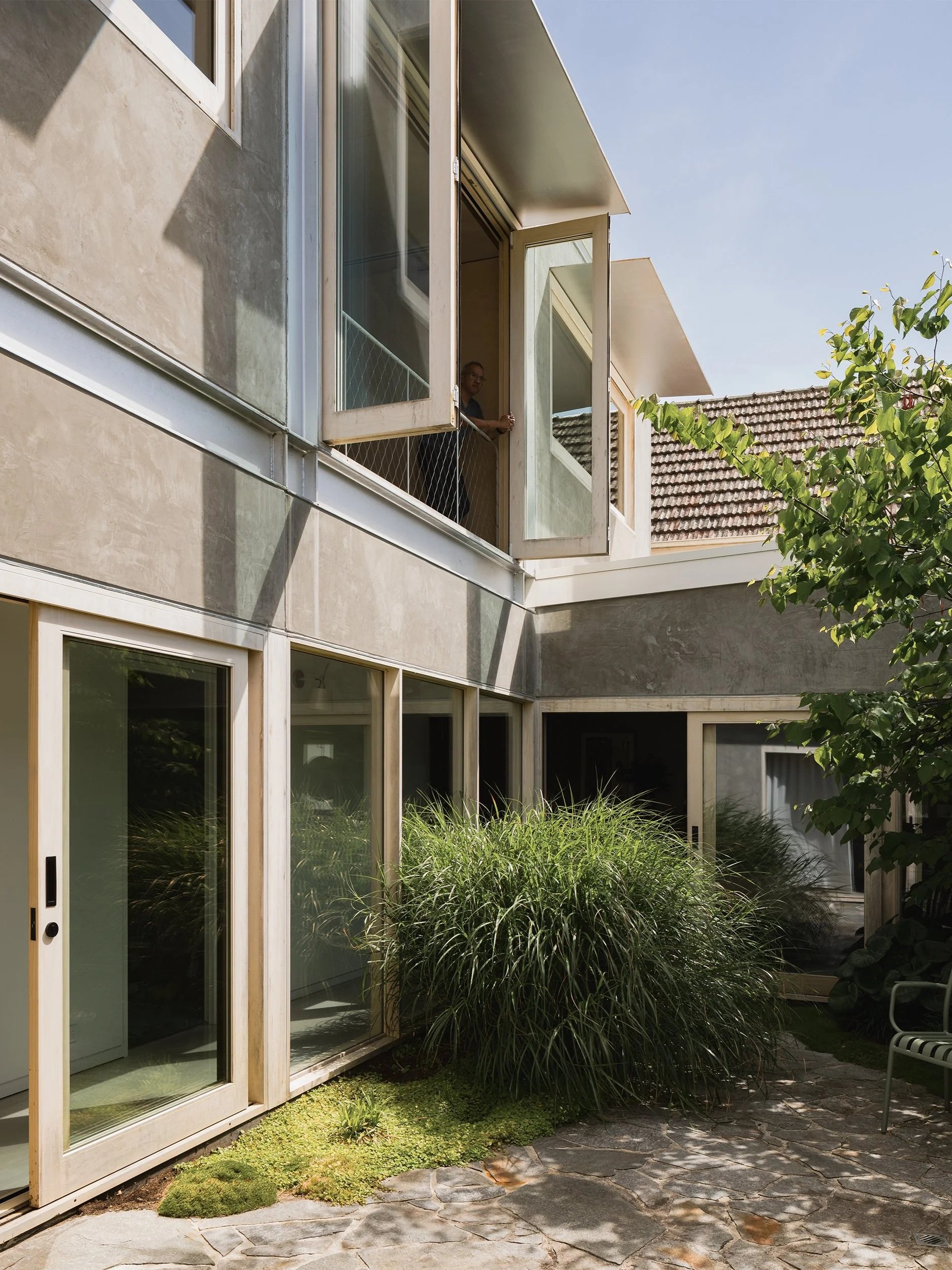 Internal courtyard at Connected House with dense grasses, timber-framed glazing and rendered Modernist walls.