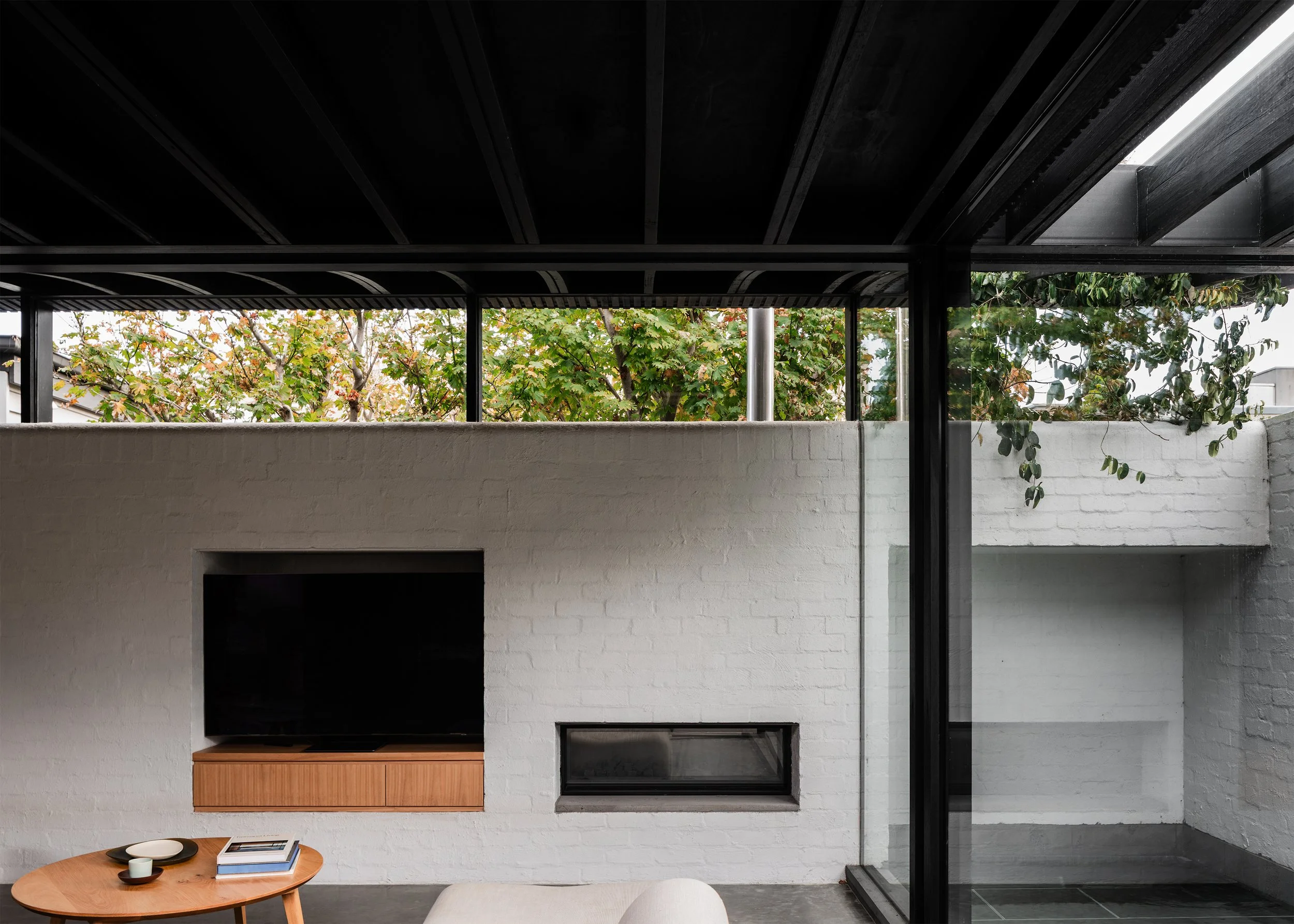 Living room glazing and white masonry garden wall framing neighbouring tree canopy beyond the site boundary.