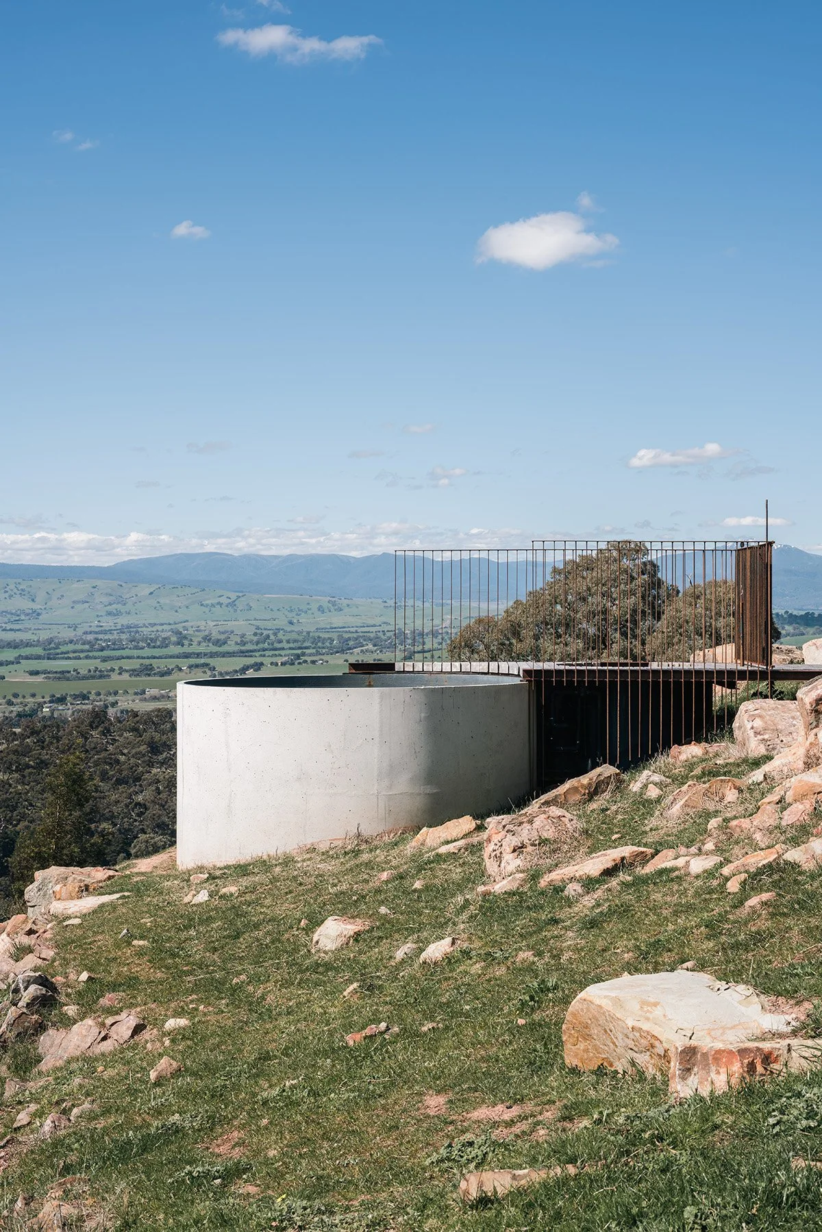 Concrete swimming pool structure and steel-railed terrace set into the rocky hill beside Mansfield House in regional Victoria.