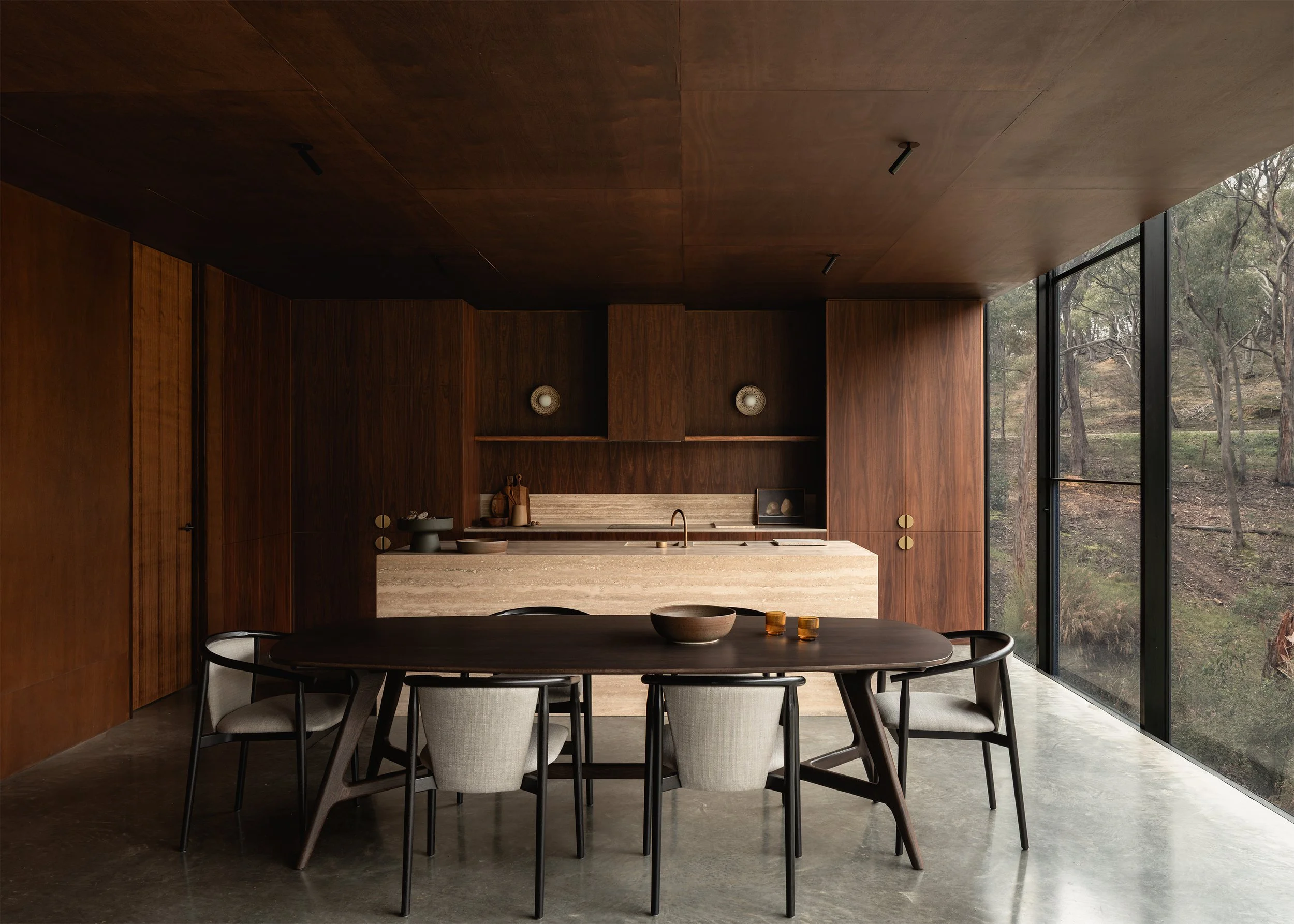 Open-plan kitchen and dining room at Matchbox, combining dark timber joinery, a travertine island and bush views.