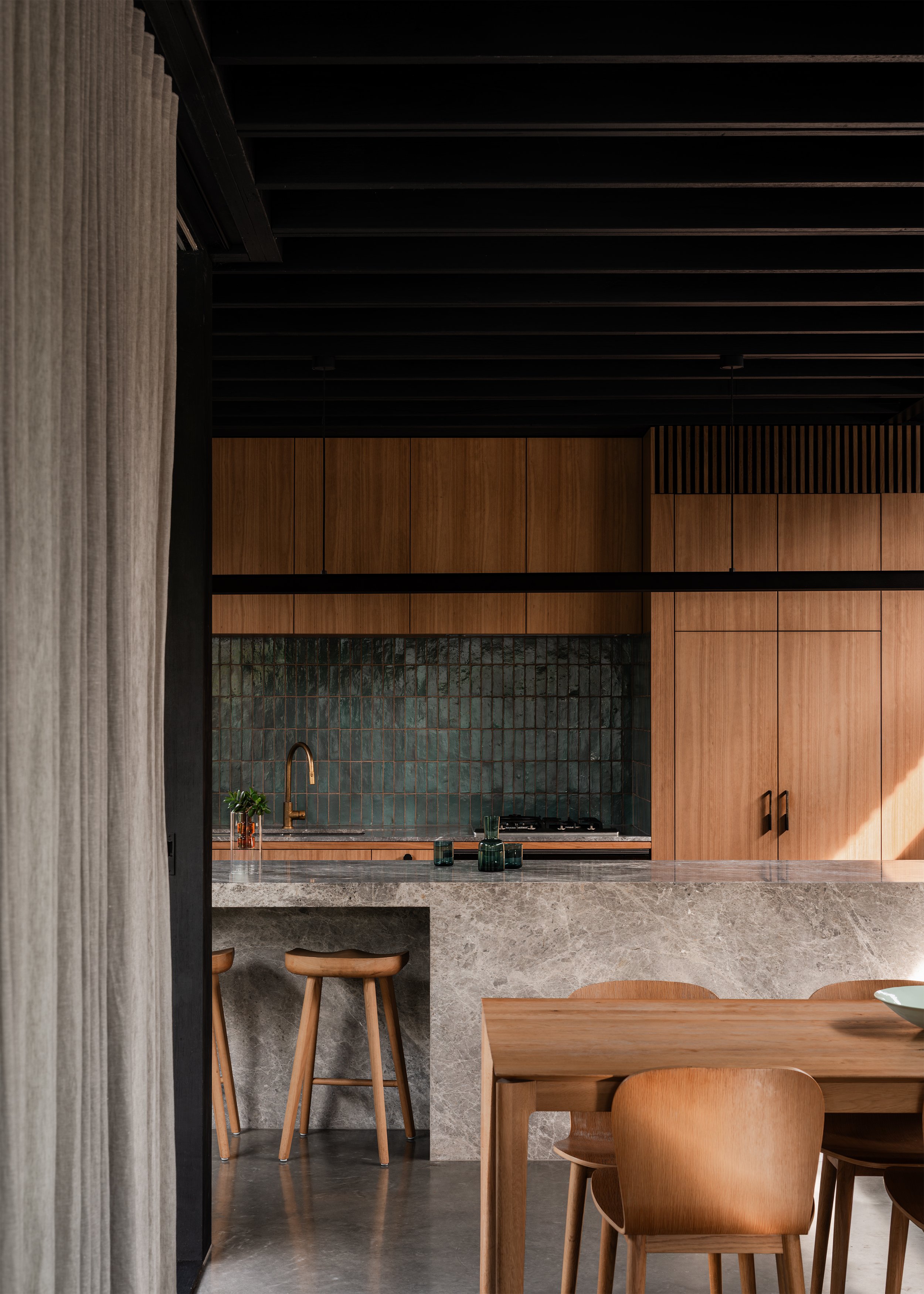 Timber kitchen and dining area with stone island, dark tiled splashback and restrained material palette.
