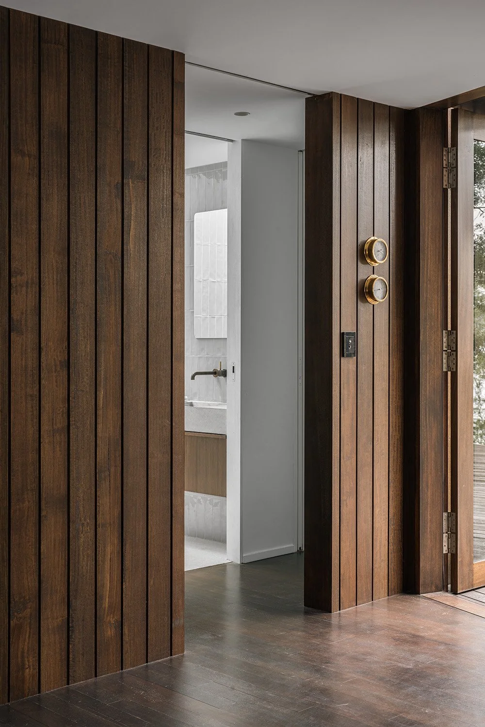 Entry and mudroom at Killora Bay, where Tasmanian timber wall linings continue toward a light-filled tiled bathroom.