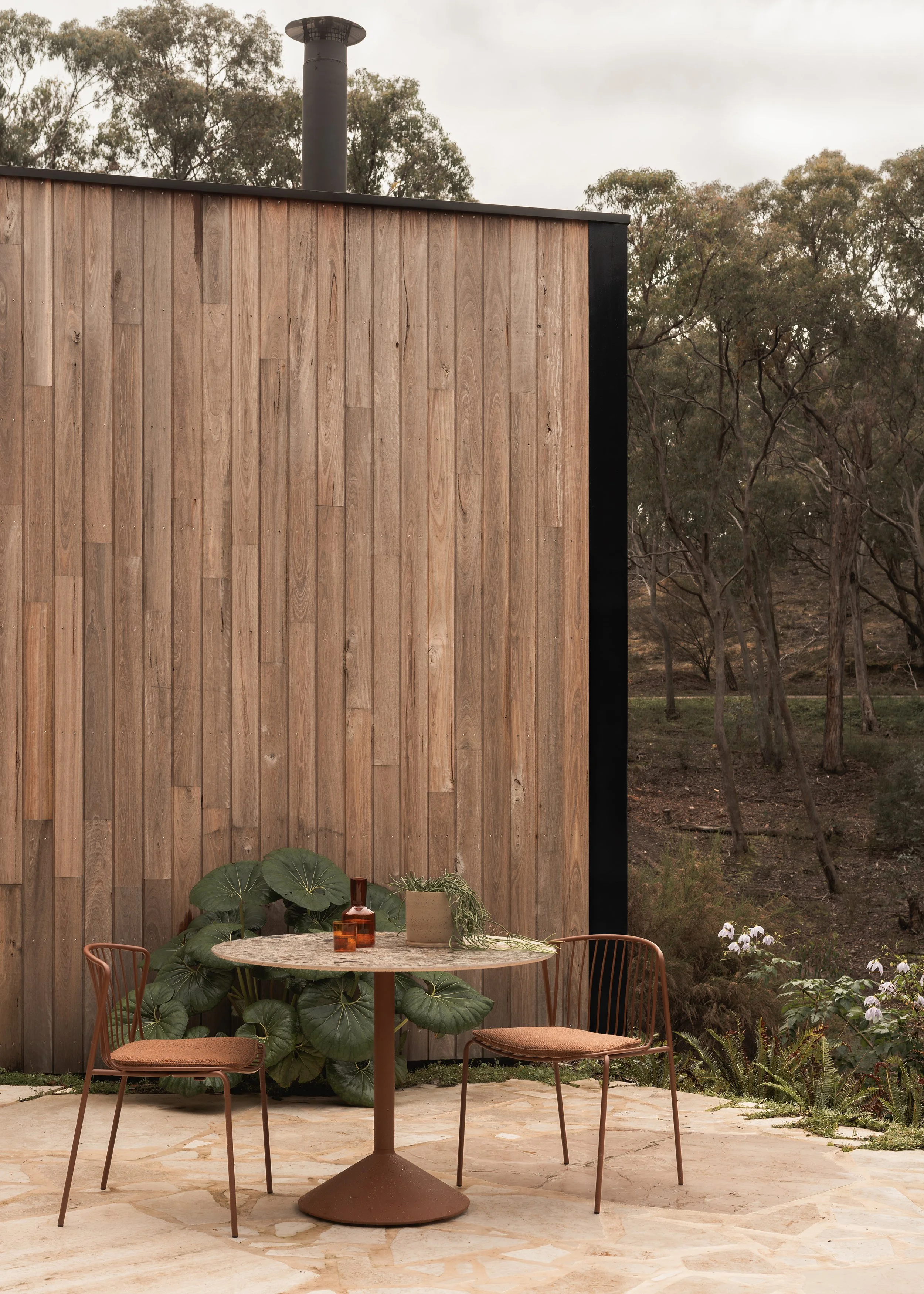 Outdoor terrace beside the timber-clad wall of Matchbox, with Cosh Living outdoor chairs and table overlooking the bushland.