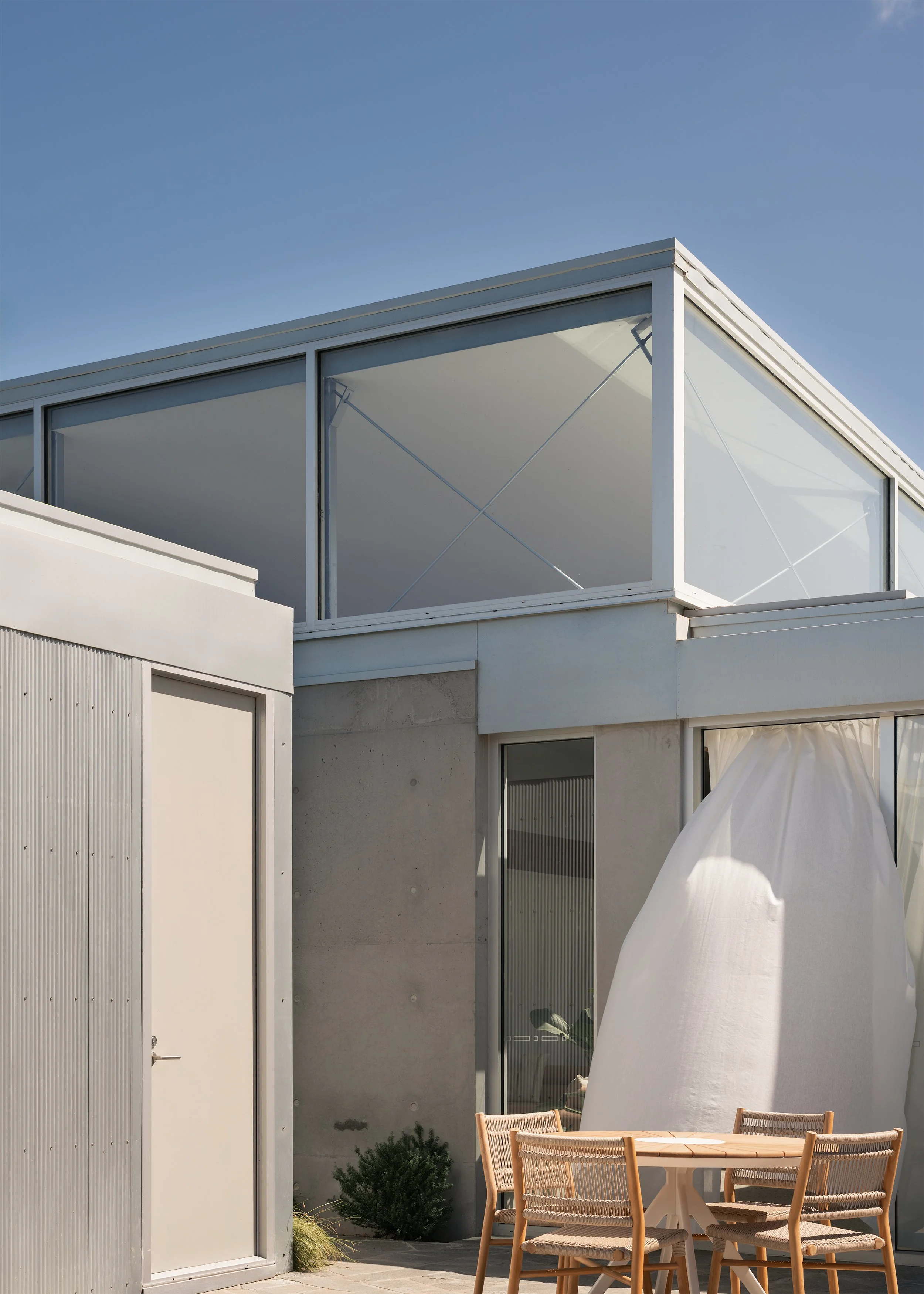 Outdoor dining courtyard beneath high-level glazing, with exposed concrete and corrugated cladding at Channel.