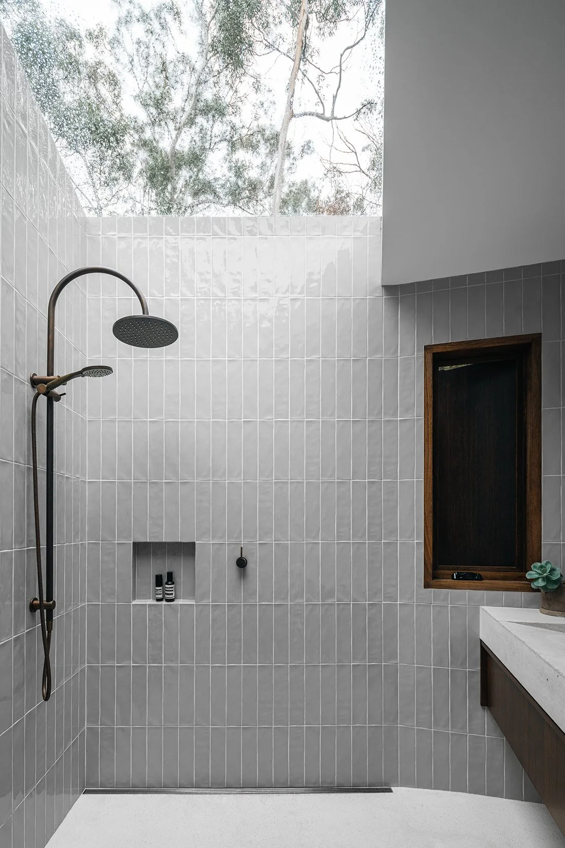 Skylit shower at Killora Bay with grey vertical tiles, dark metal fittings and views to the surrounding gum-tree canopy