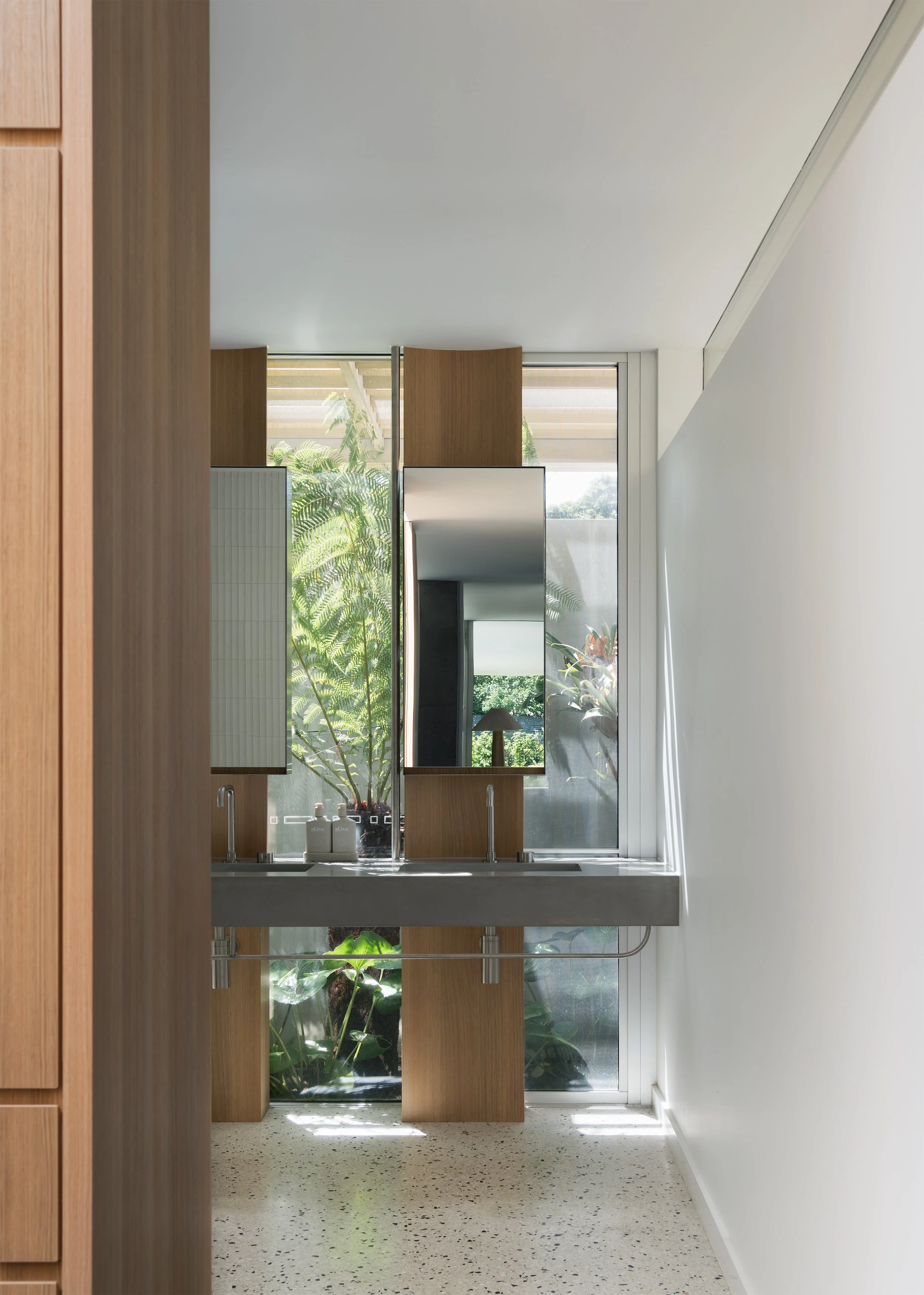 Double bathroom vanity framed by floor-to-ceiling glazing and dense garden planting at Channel by Megowan Architectural.